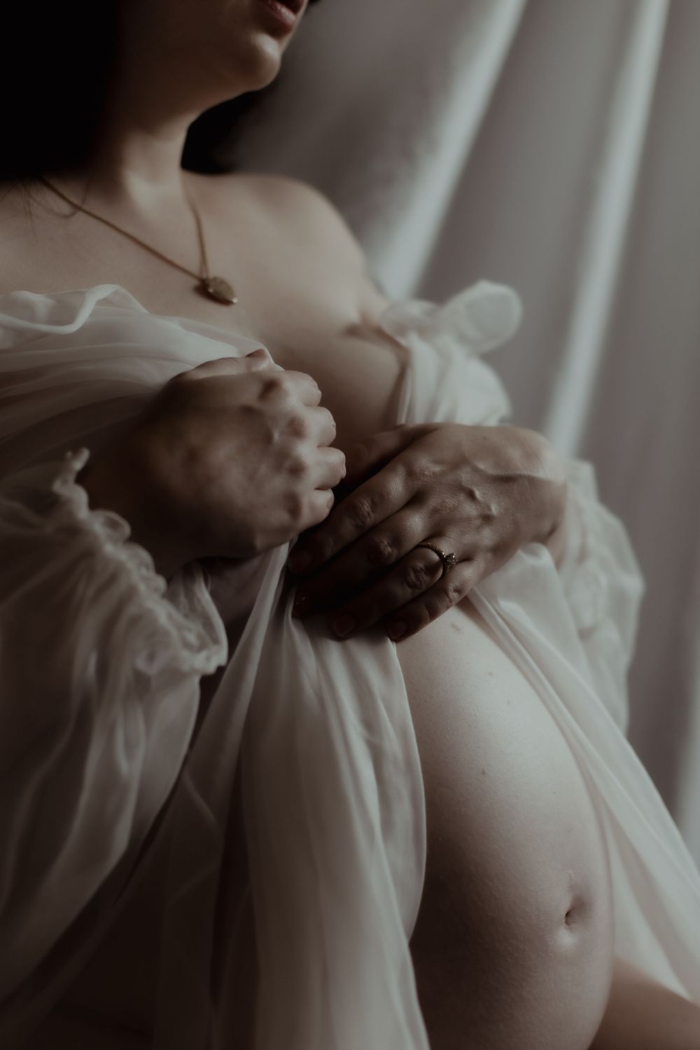 An artistic close-up of a woman's hands resting on white fabric in soft natural light. PNW Maternity Photographer