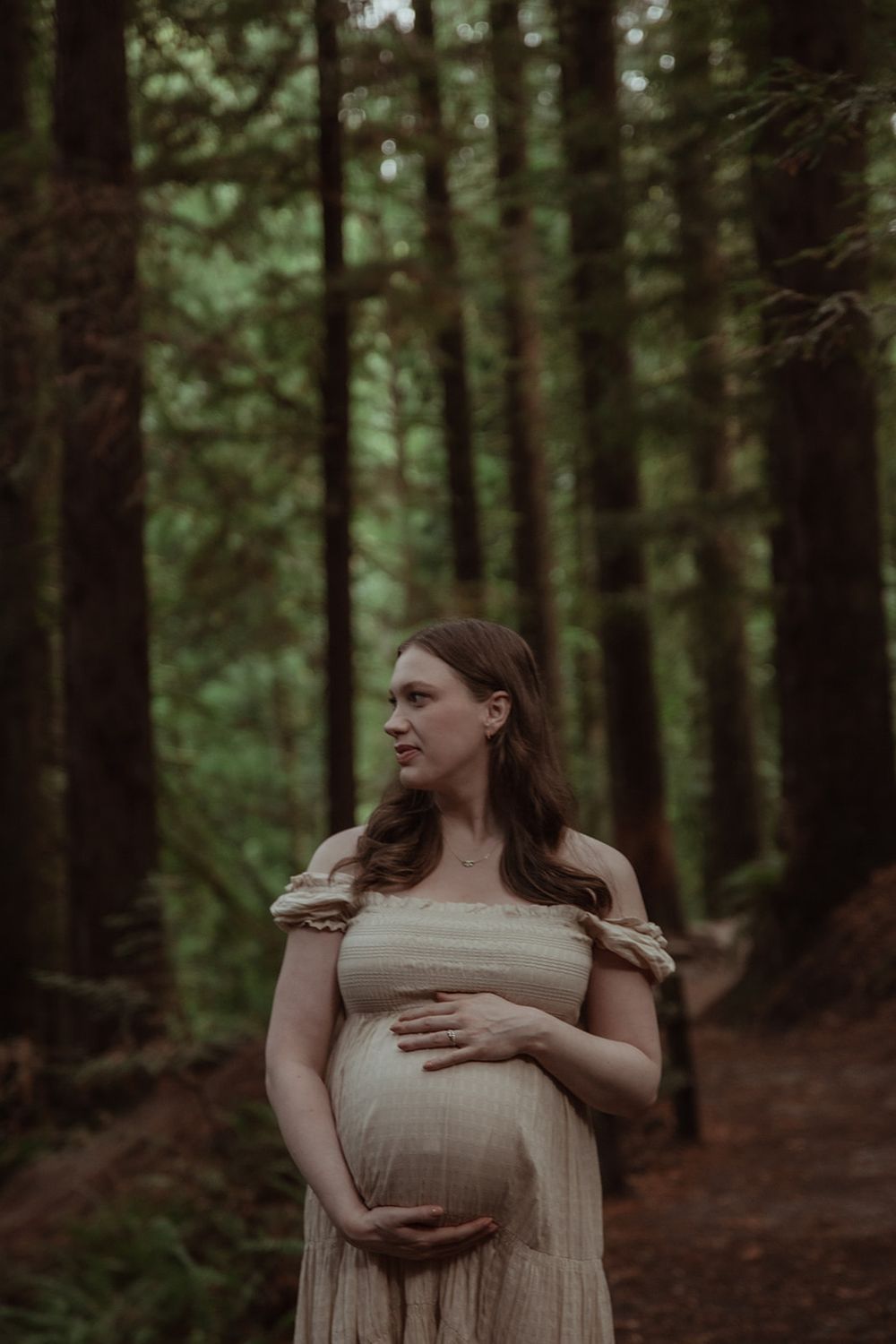 Maternity photo of woman in flowing dress standing in forest. PNW Maternity Photographer