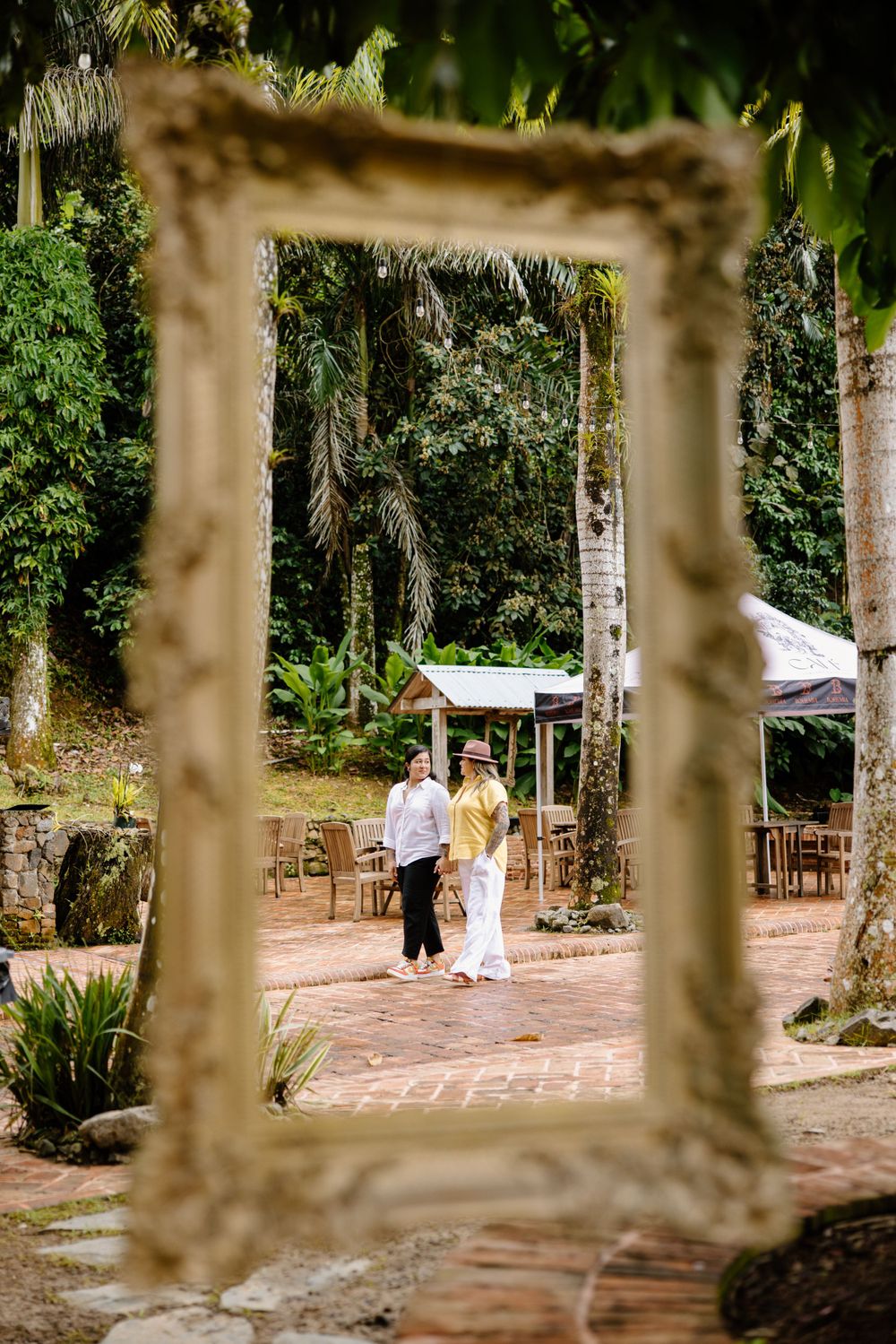A romantic garden setting framed through an ornate picture frame with a couple walking on a stone path.