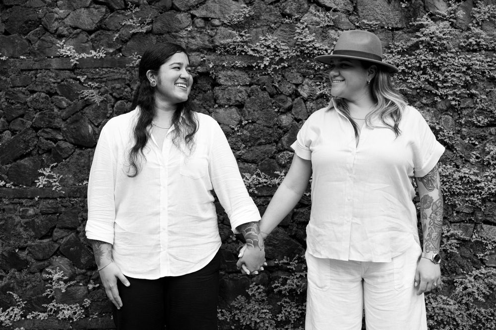 Two people in white outfits share a tender moment against a rustic stone wall.