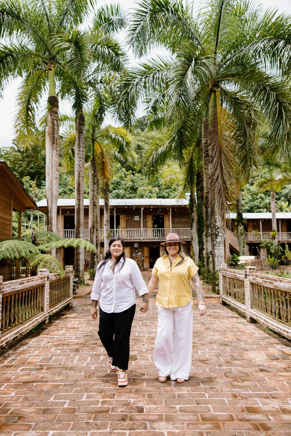 Two people walking together on a brick pathway lined with tall royal palm trees.