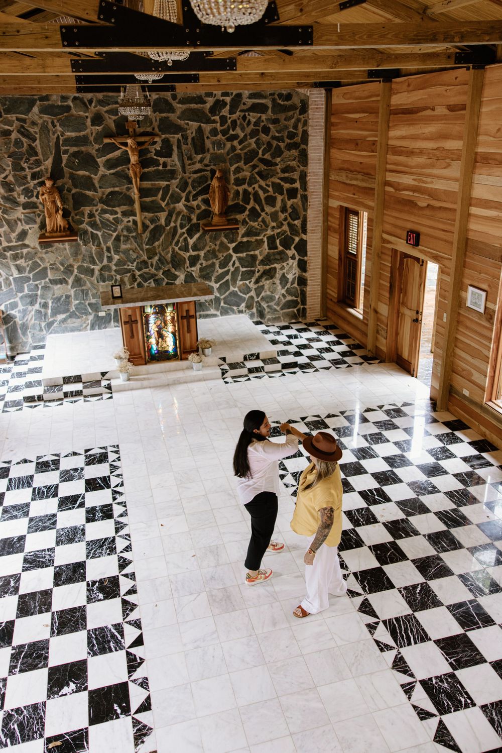 Two people dancing together on a checkered floor in a rustic stone and wood interior.