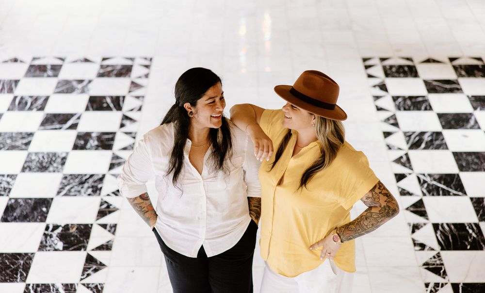 Two people sharing a laugh on black and white checkered floor with photo wall behind them.