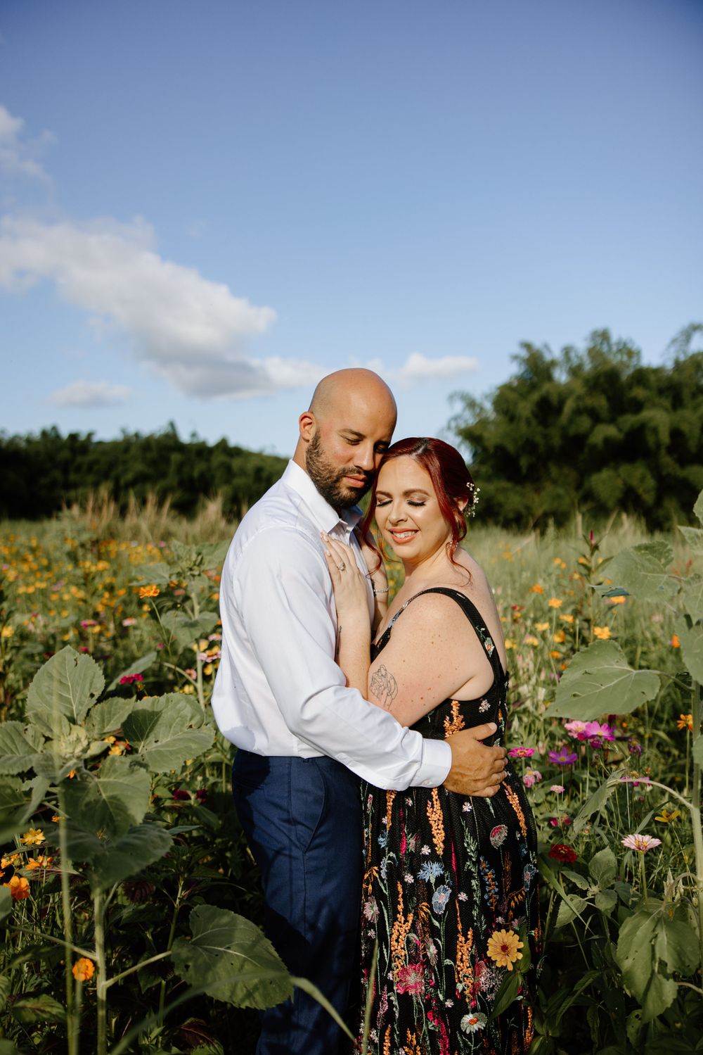A couple embraces among blooming sunflowers and wildflowers on a sunny day.