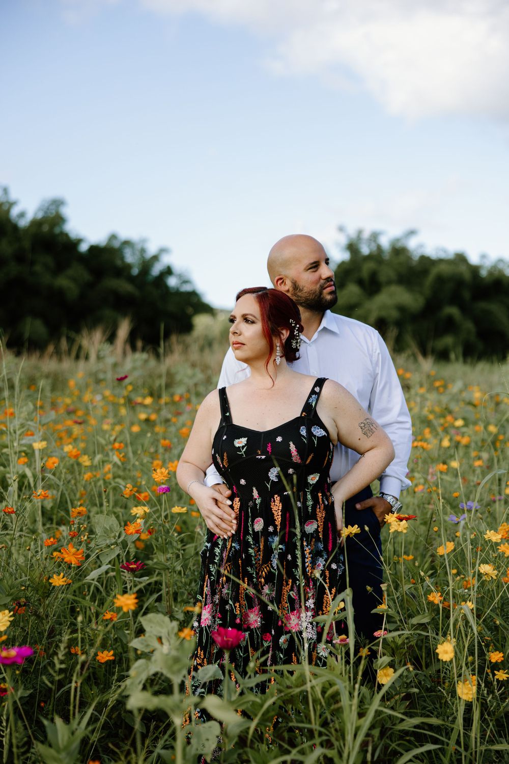 A couple stands together in a field of vibrant yellow and pink wildflowers.