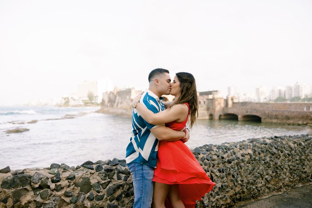 A romantic moment captured on rocky coastline with historic architecture in background.