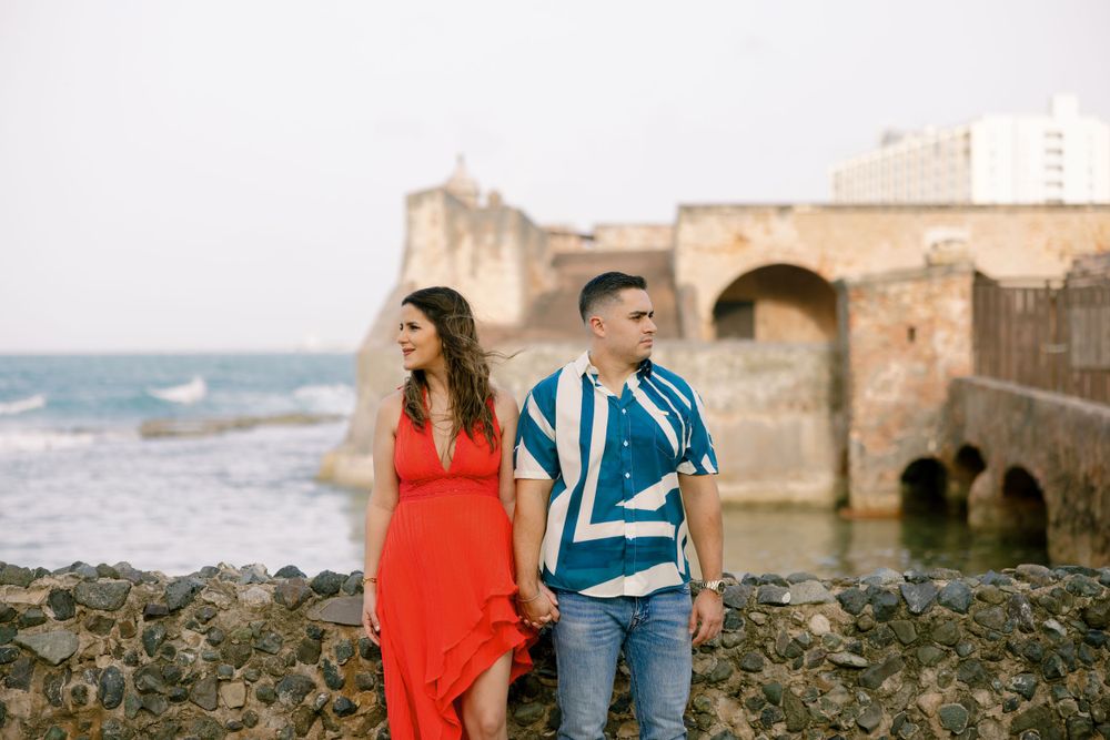 A couple posing together against an ancient stone fortress wall by the ocean.