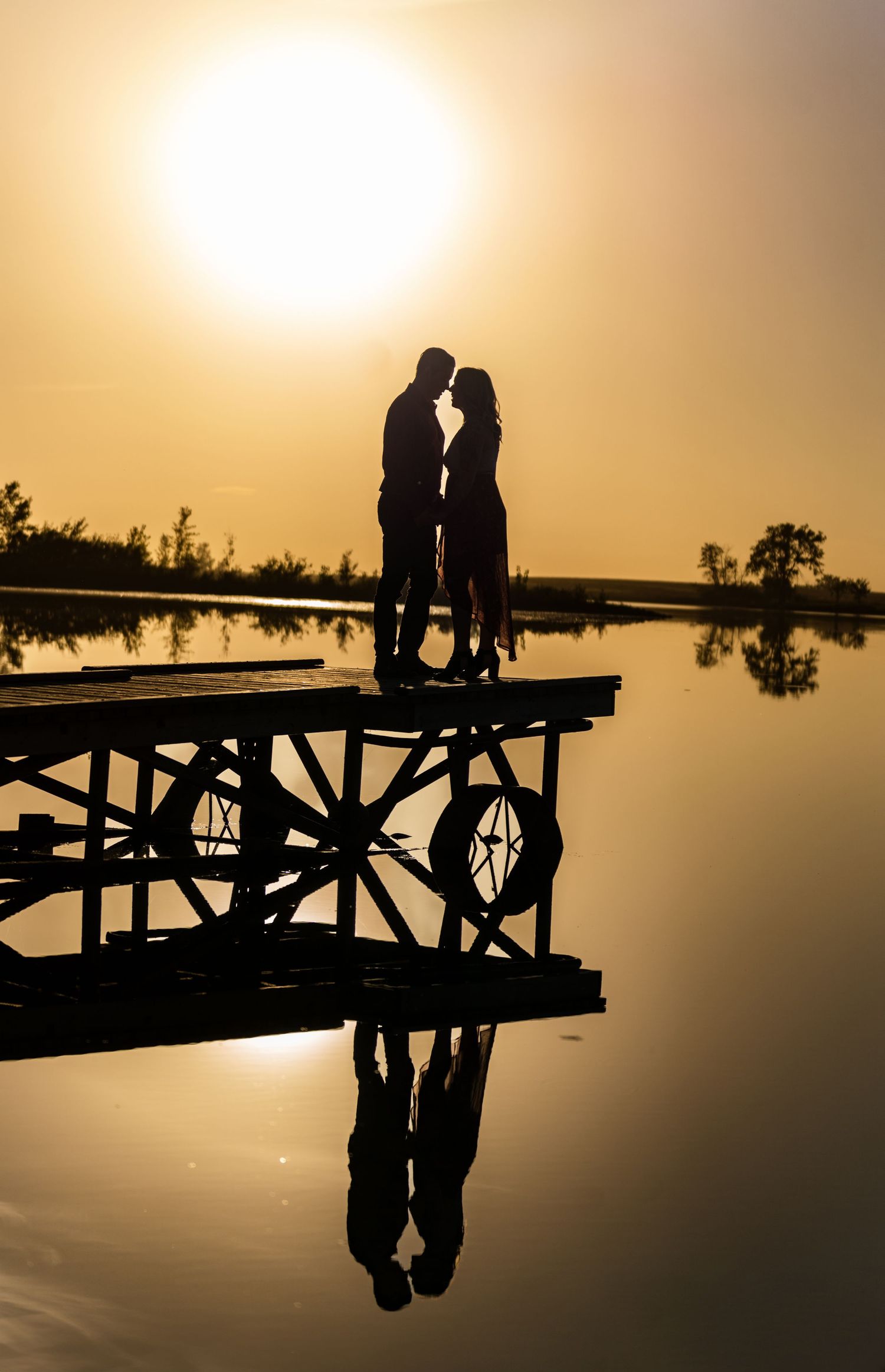 Silhouettes of a couple sitting on a dock at sunset create a romantic scene reflected in calm waters.