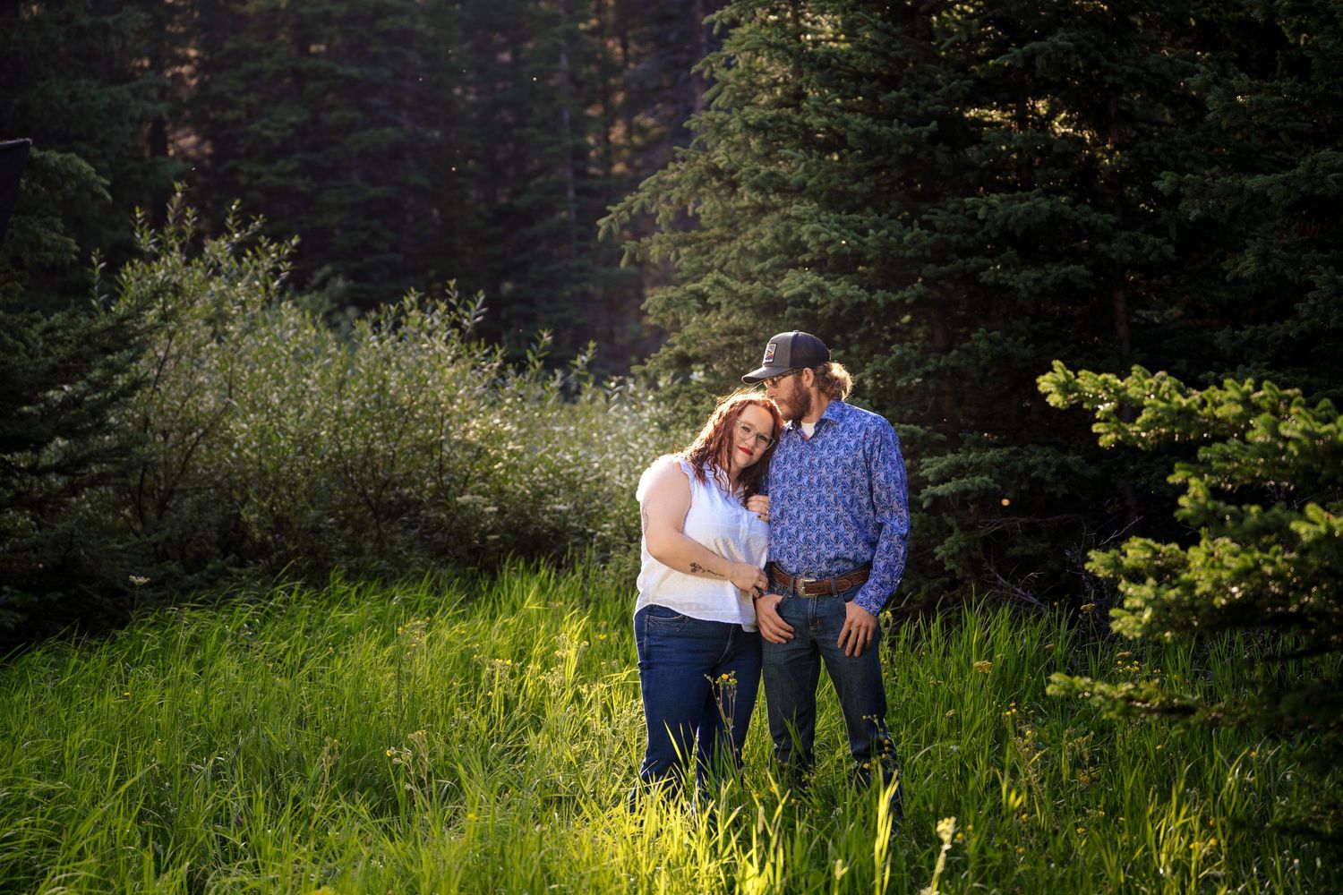 Romantic couple shares tender moments in a lush green meadow during golden hour photography session.