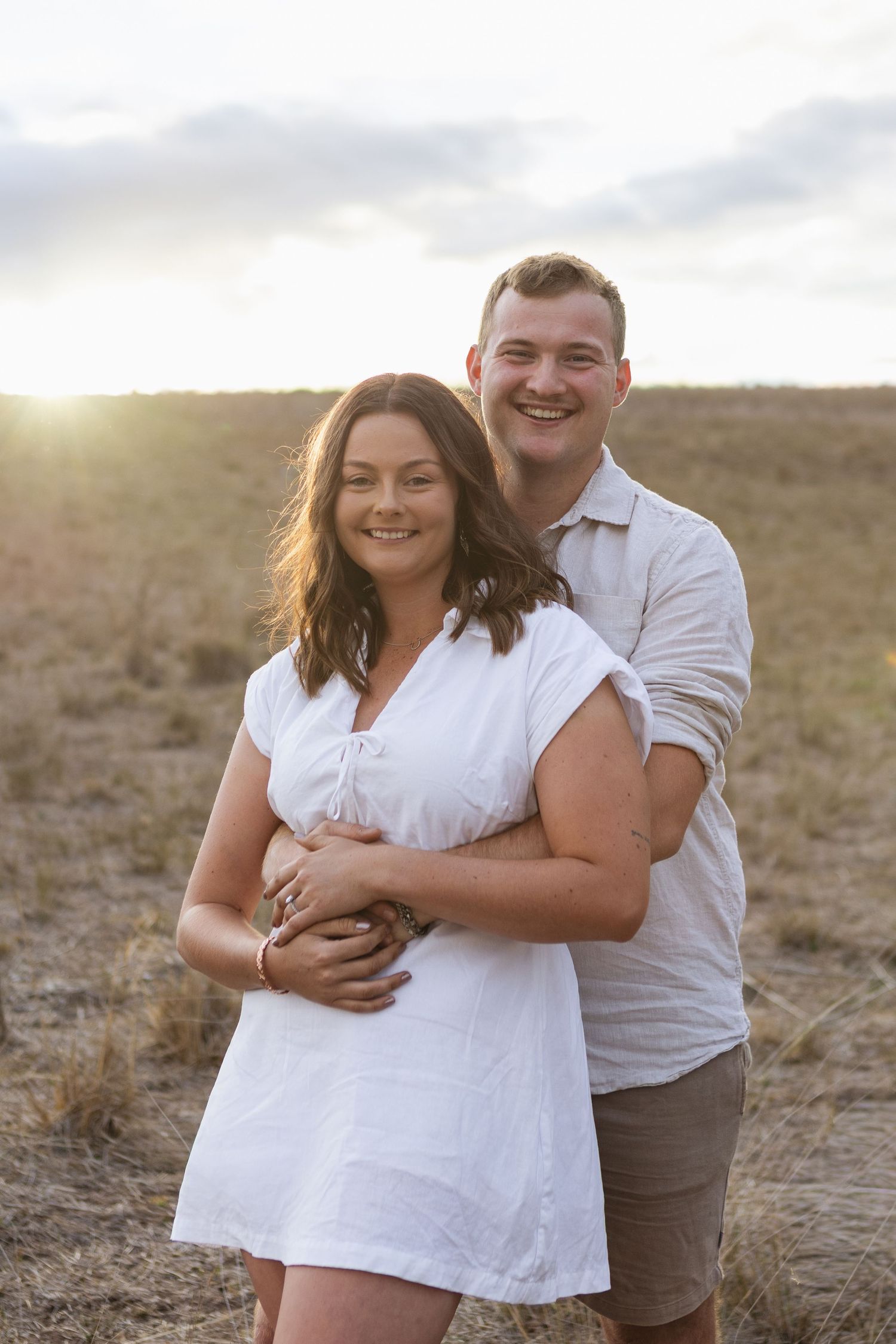 country style couple hugging from behind and smiling at camera during engagement photoshoot near Scone NSW