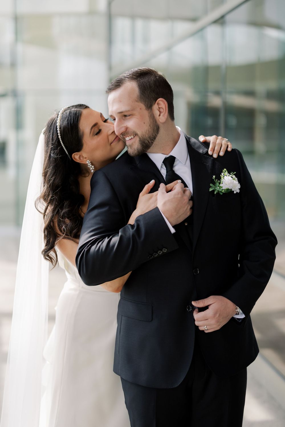 Romantic moment between newlyweds in formal attire against modern glass building background.