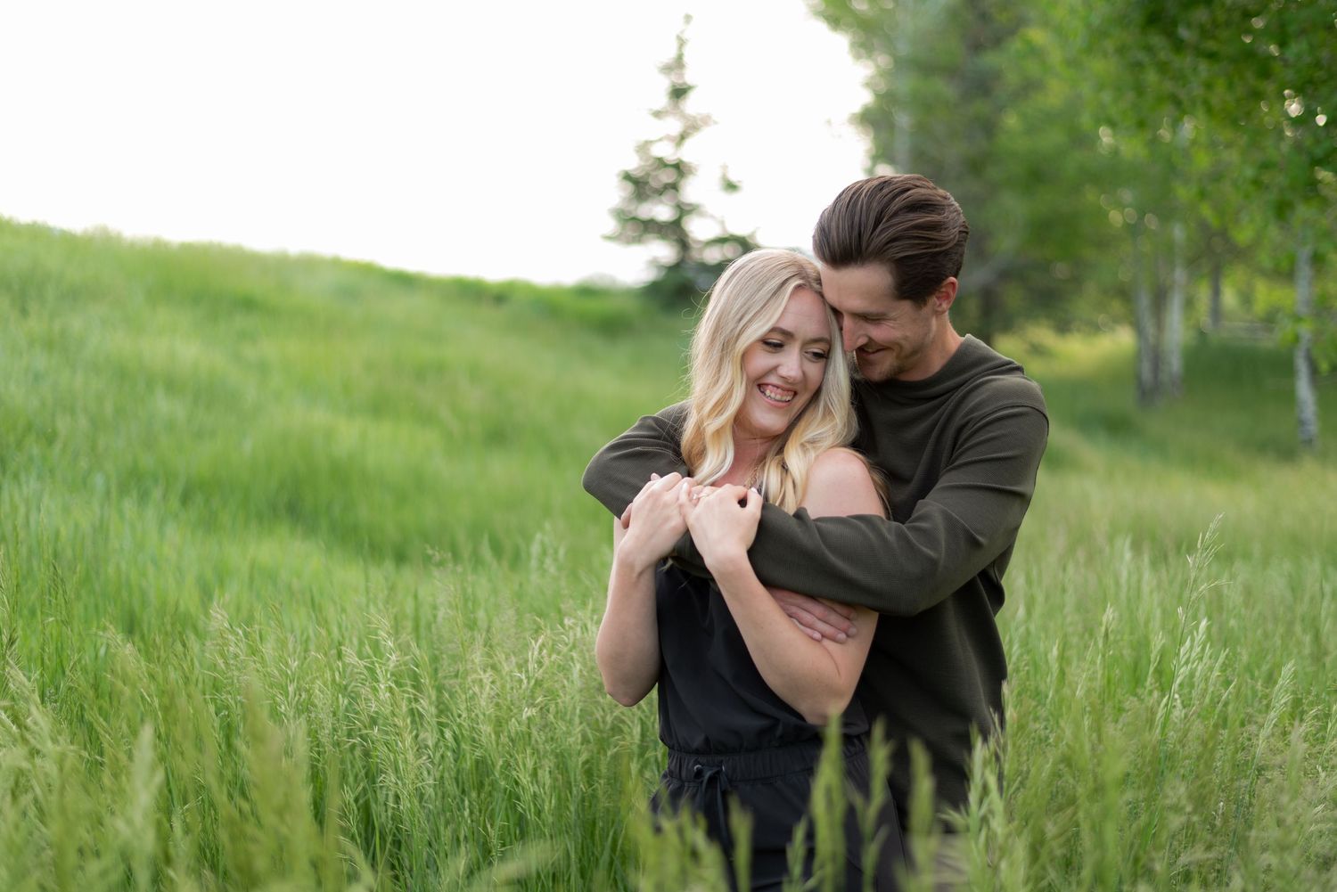 Couple embraces tenderly in a lush green meadow during a romantic outdoor photo session.