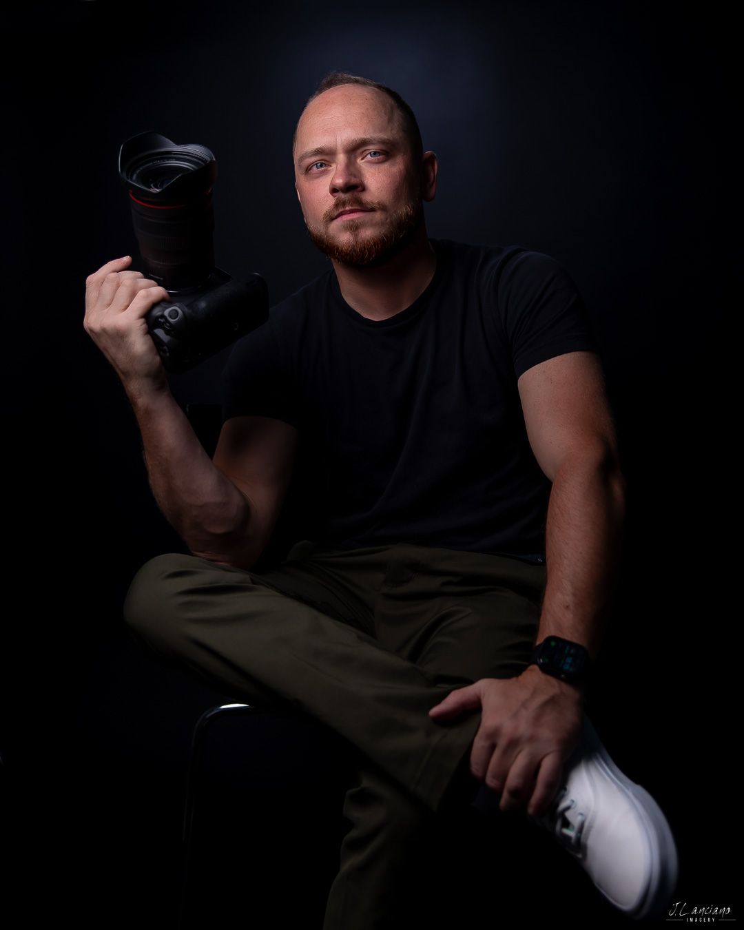 Dramatic portrait of photographer holding camera against dark background.