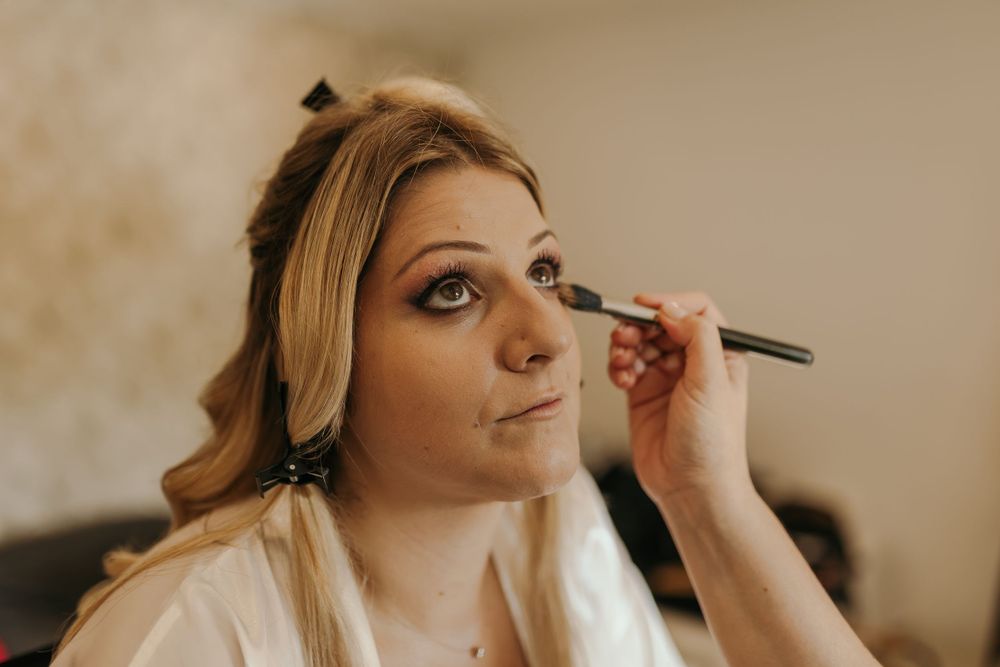 Bride getting eye makeup applied by a makeup artist during wedding preparation.