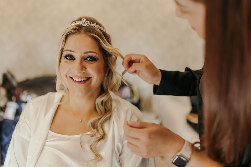 Smiling bride wearing a tiara getting her hair styled by a hairdresser during wedding preparations.