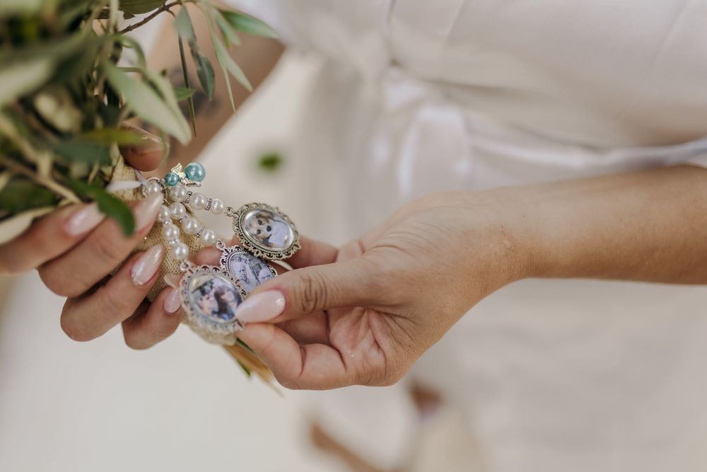 Close-up of bride holding a delicate pearl and crystal bracelet with a bouquet of greenery.