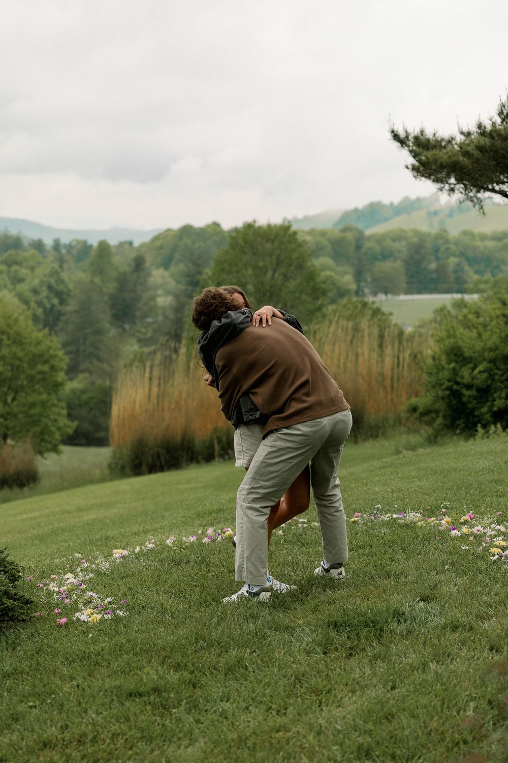 Person crouching to take photos on a scenic hilltop with mountain views.