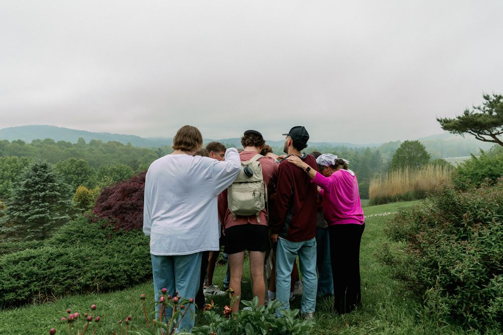 A group of friends pray together while enjoying a mountaintop view on an overcast day.