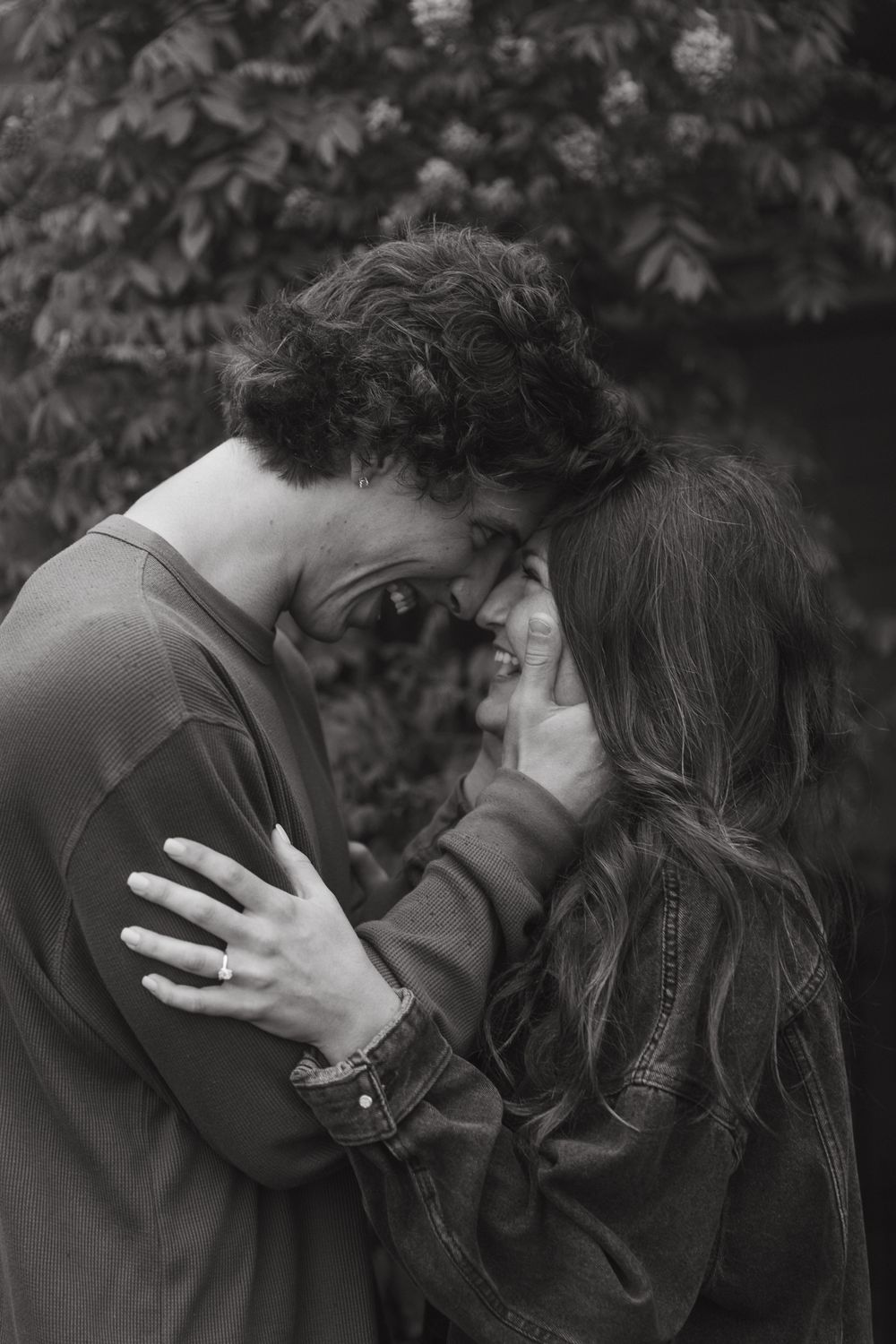 A tender black and white portrait of a couple sharing an intimate moment among foliage.