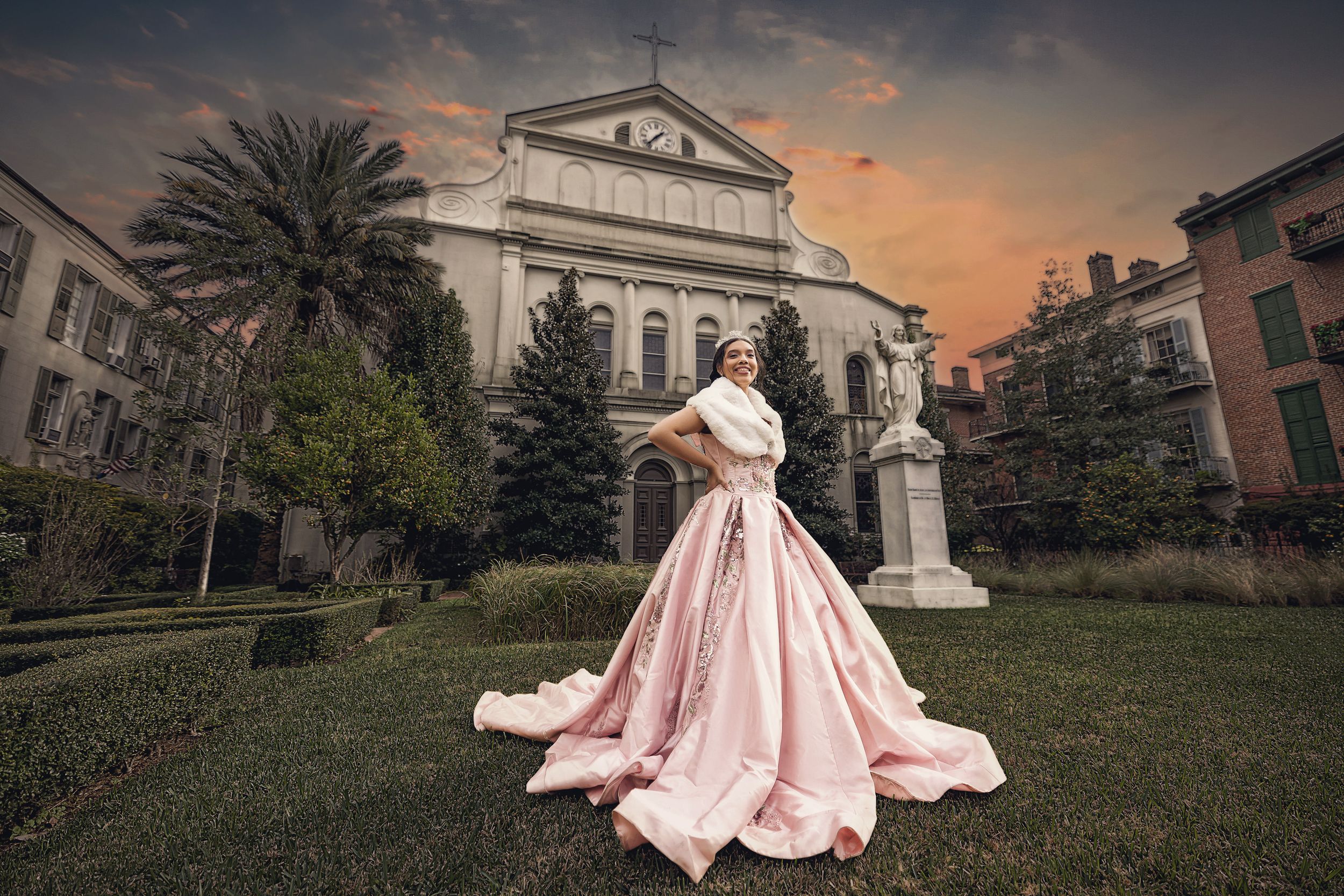 Quinceañera in a blush pink gown on a lawn in front of a historic building