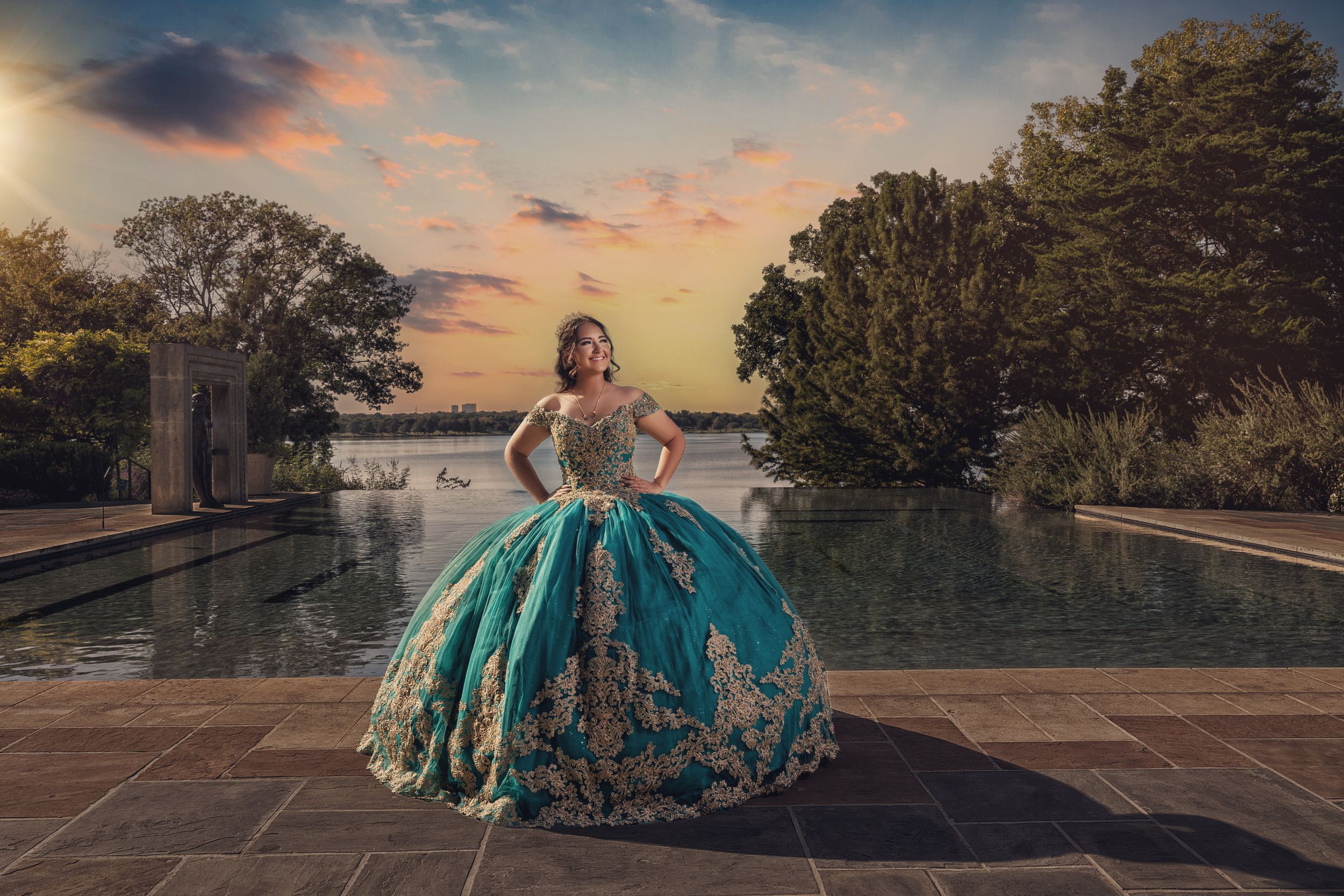 Quinceañera in a teal and gold gown beside the water at sunset