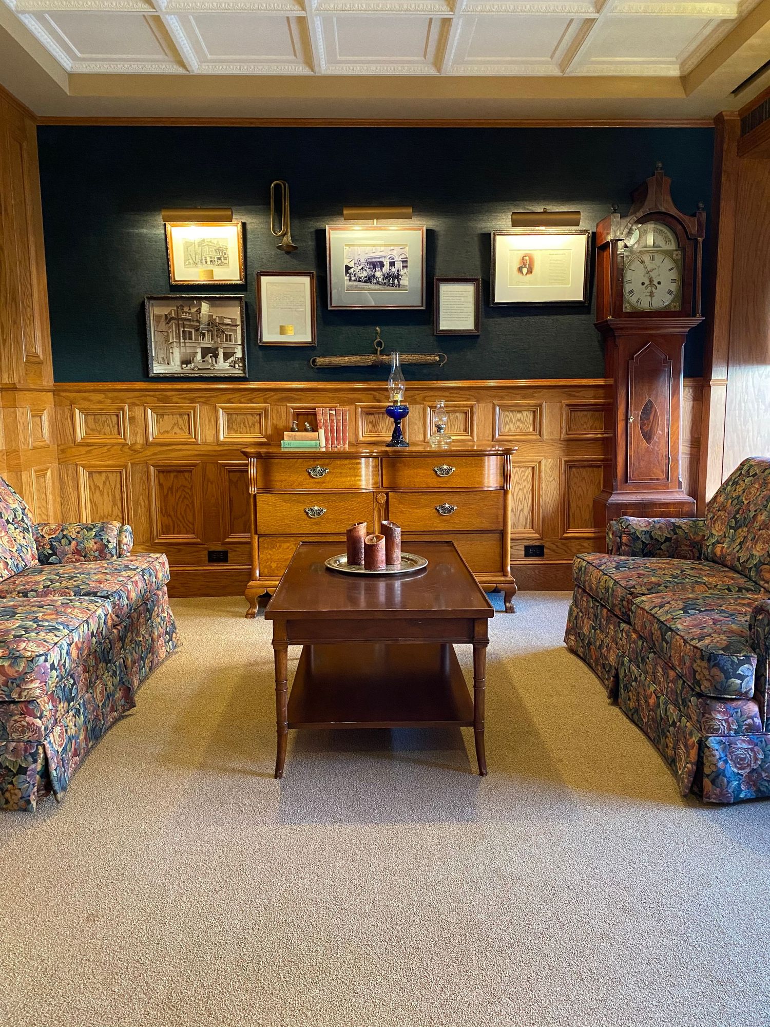 Traditional wood-paneled room with floral sofas, grandfather clock and framed artwork.