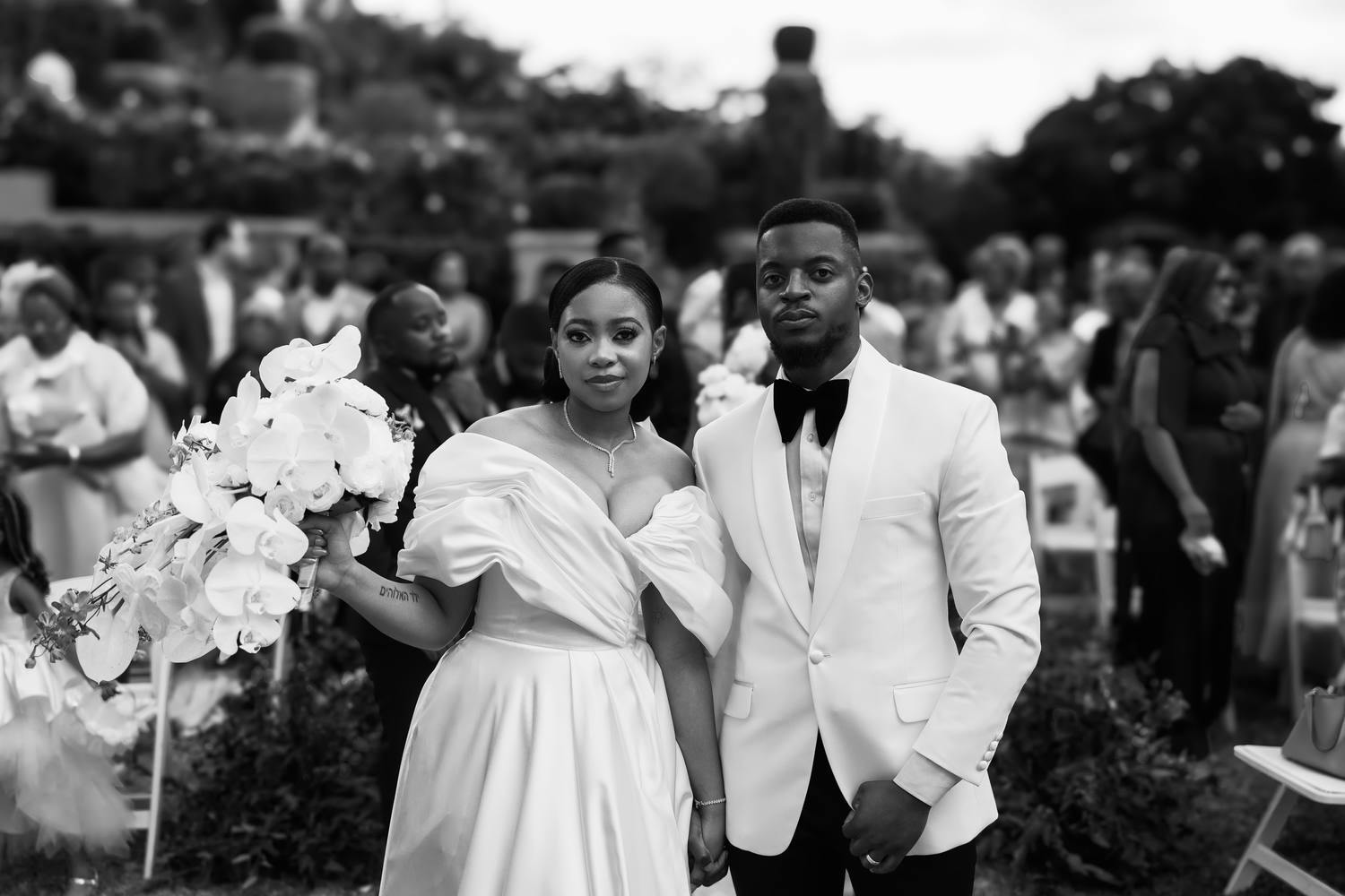 Black and white wedding photo of a couple in formal attire with floral arrangements.