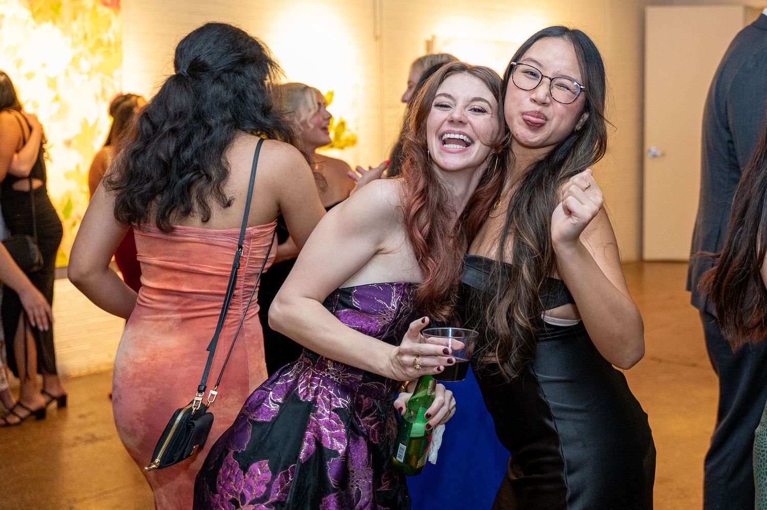 Two women pose for a fun photo while wearing formal dresses.