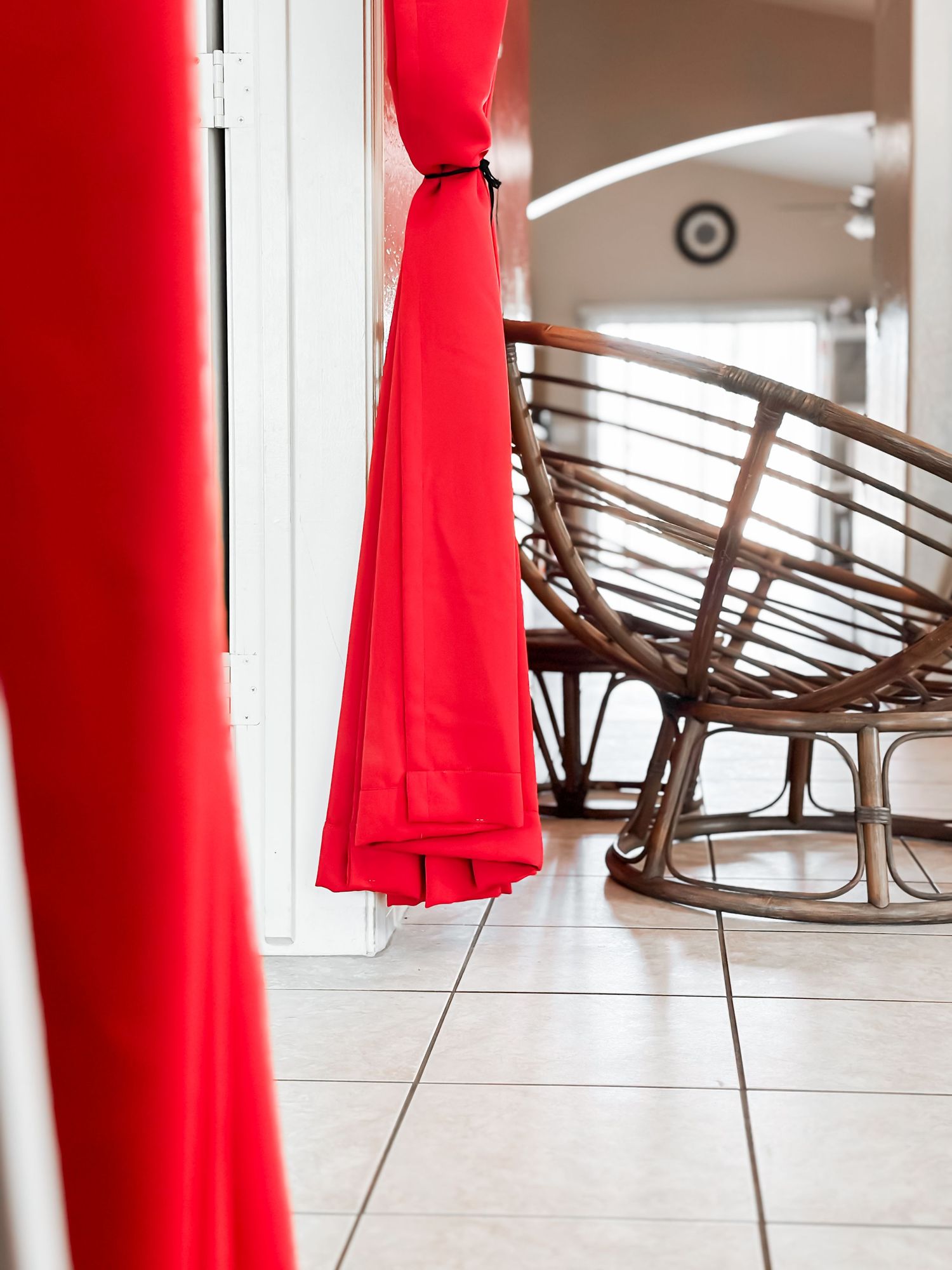 Red curtain detail with rattan rocking chair in corner of tiled room.