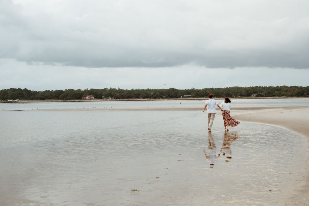 A couple plays together at the water's edge on an overcast beach day.