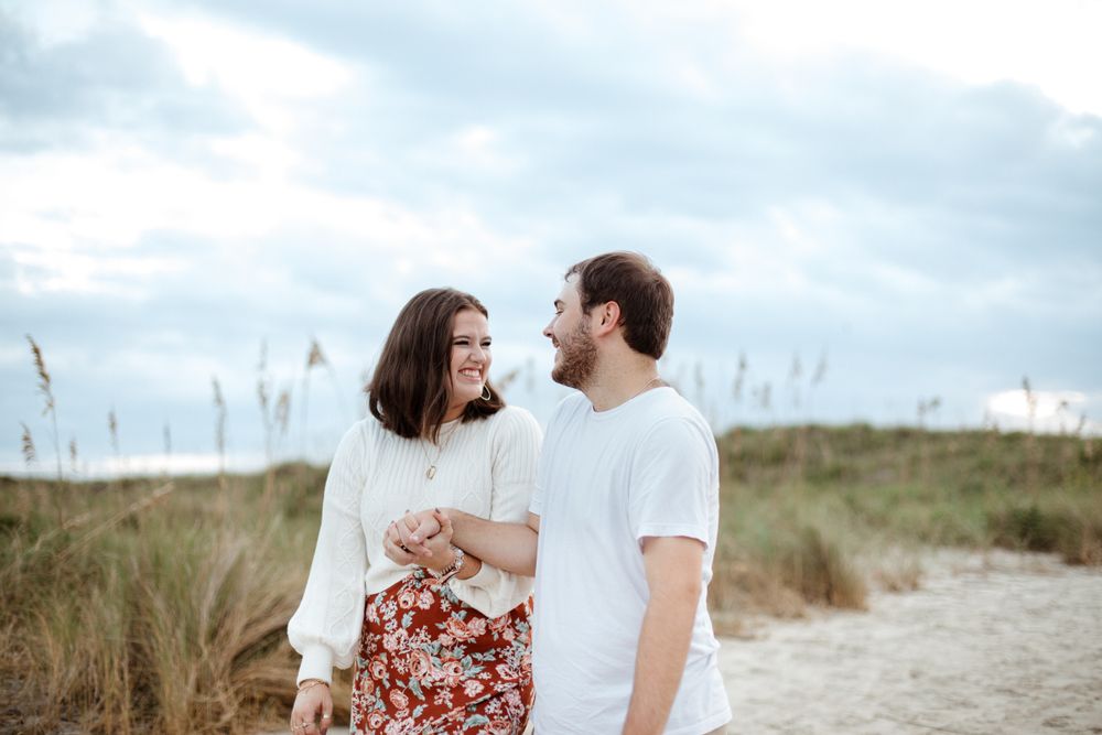 Couple in white outfits sharing intimate moments on a sandy beach with sea grass.