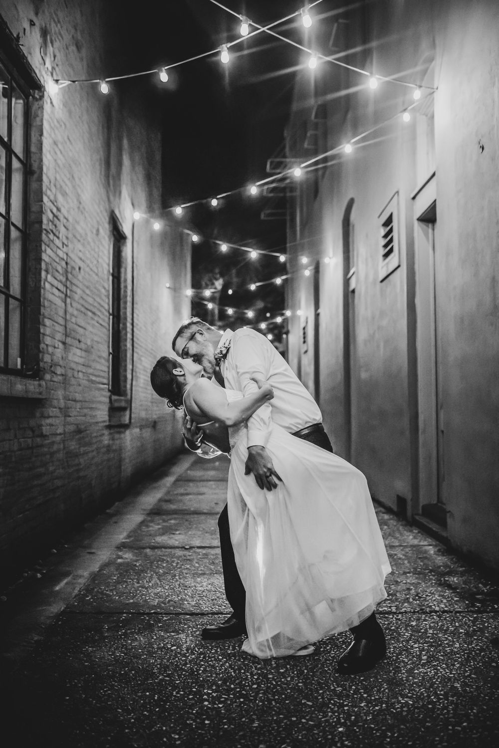 A romantic black and white photo taken in an alley at night with string lights overhead.