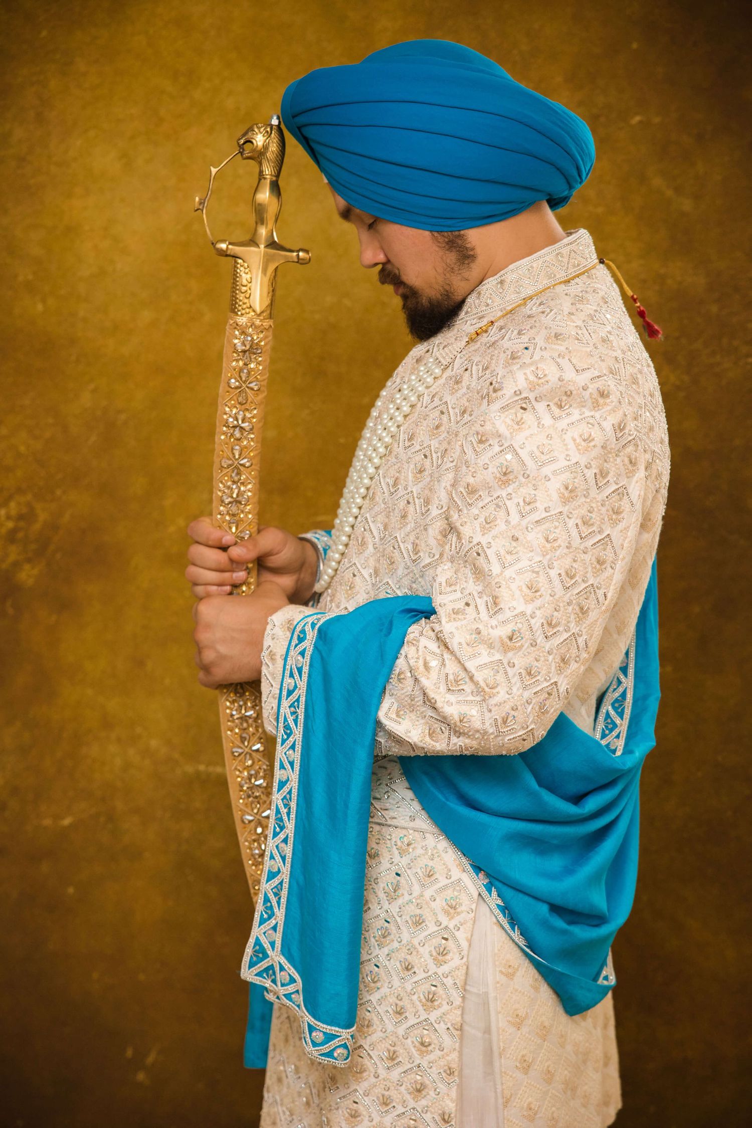A Sikh groom posing infront of a kirpan, wearing a white luxury Kurta