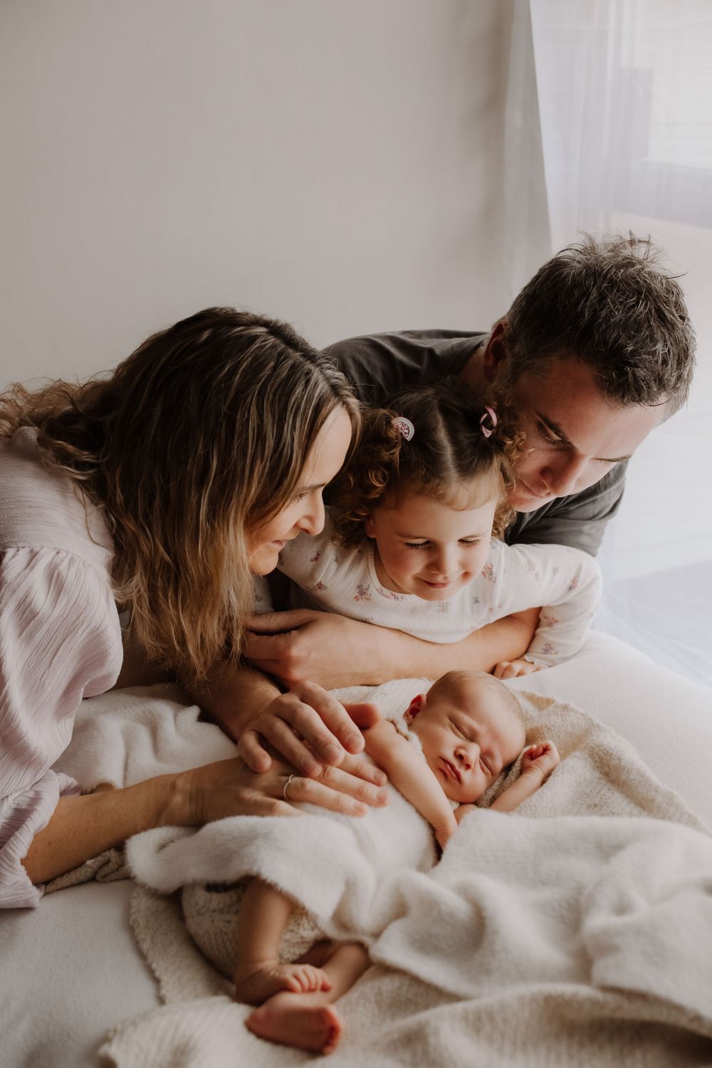 Parents cuddling their newborn baby during a cozy in-home lifestyle photography session in Westport. Big sister meeting her newborn sibling