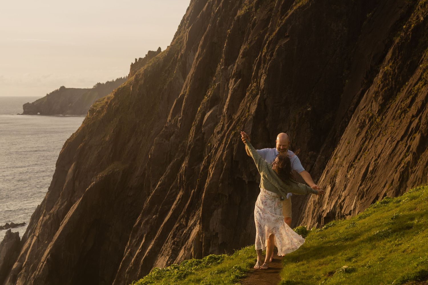 A couple embraces while looking out over a scenic overlook at sunset with a misty sky and water view.