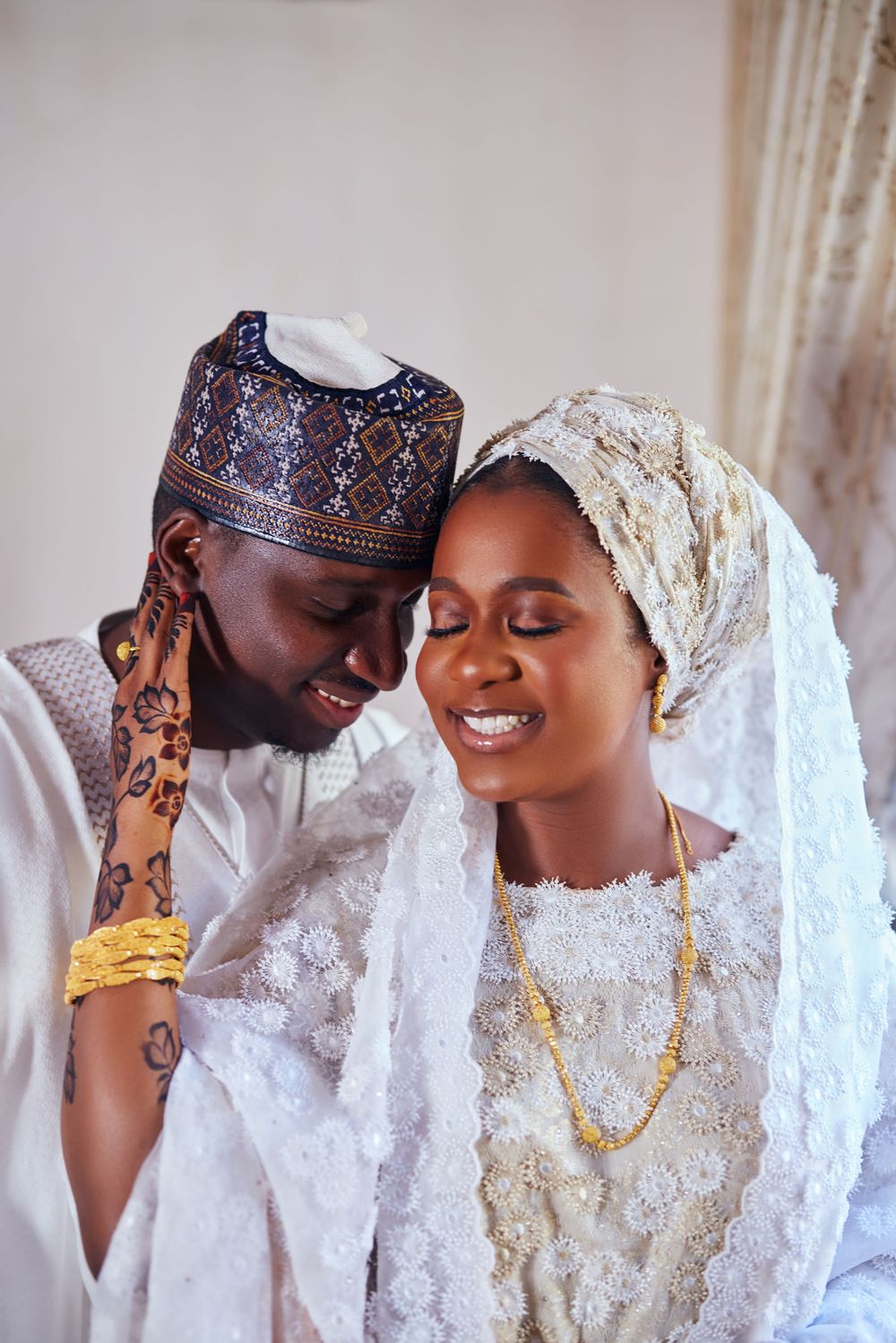 Joyful couple in traditional white wedding attire sharing intimate moment with henna details.