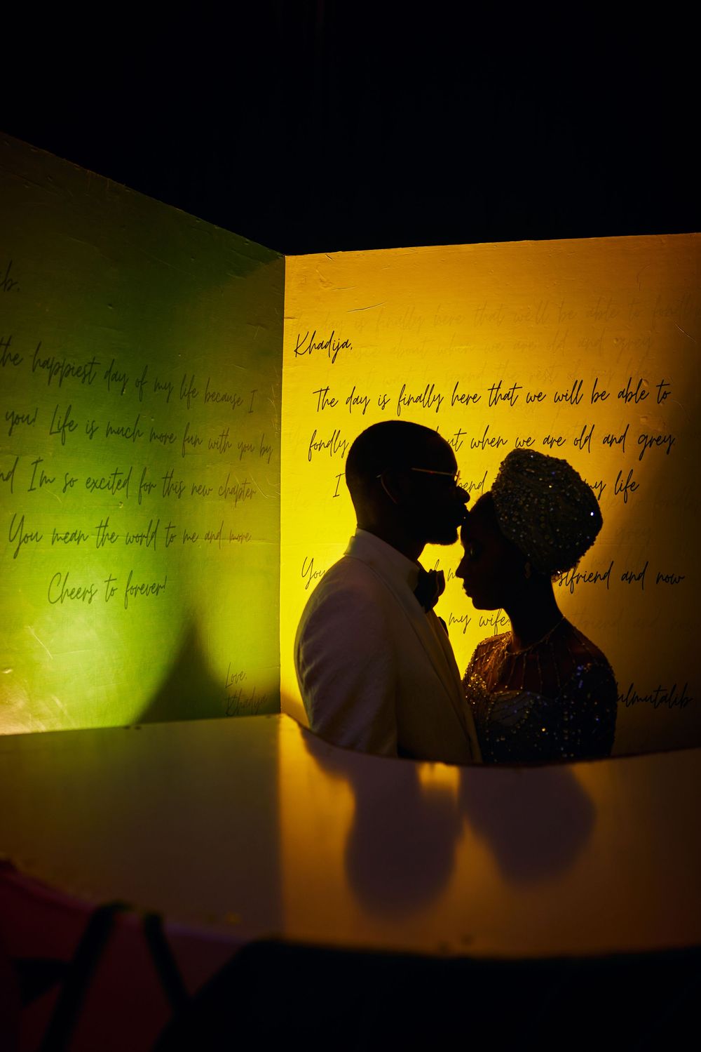 Romantic silhouette of couple against yellow and green wall with handwritten text.