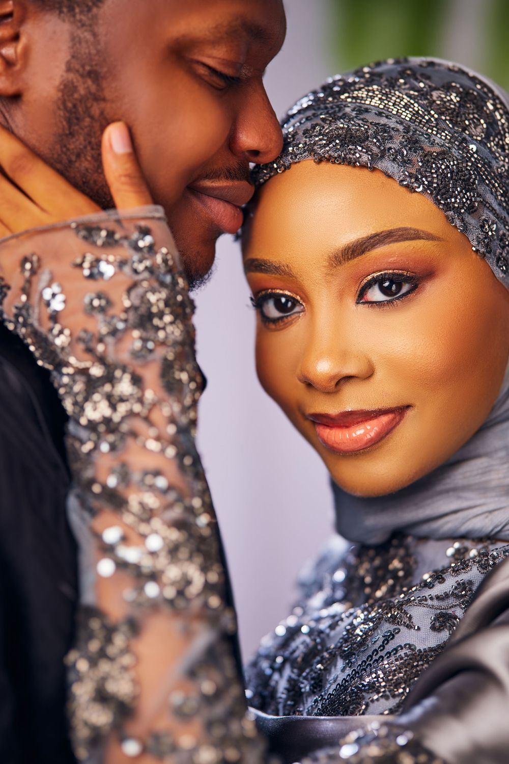 Intimate portrait of couple in sparkling formal wear and hijab against light background.