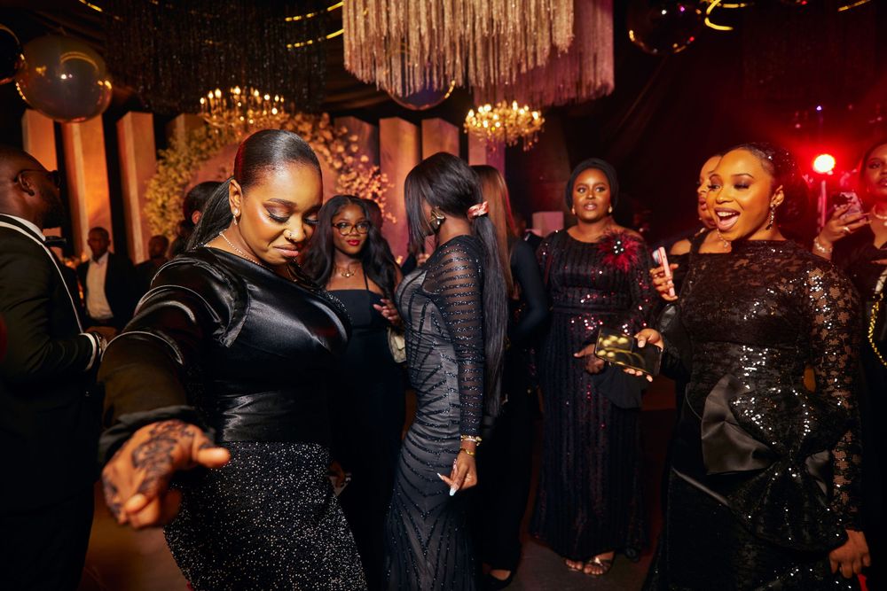 Elegantly dressed guests dancing and socializing at reception under crystal chandeliers.