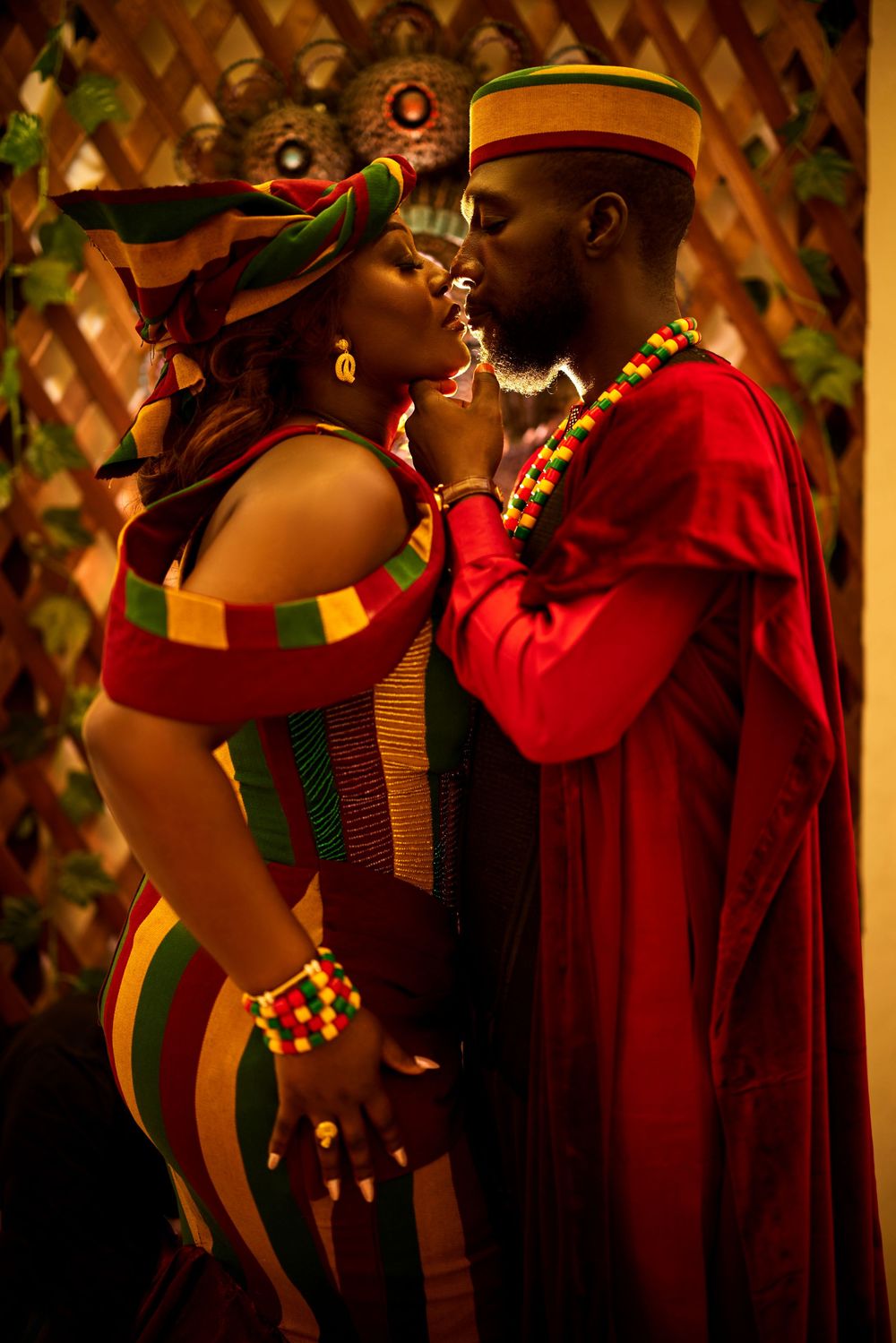 Couple in vibrant African-inspired attire sharing an intimate moment against decorative backdrop.