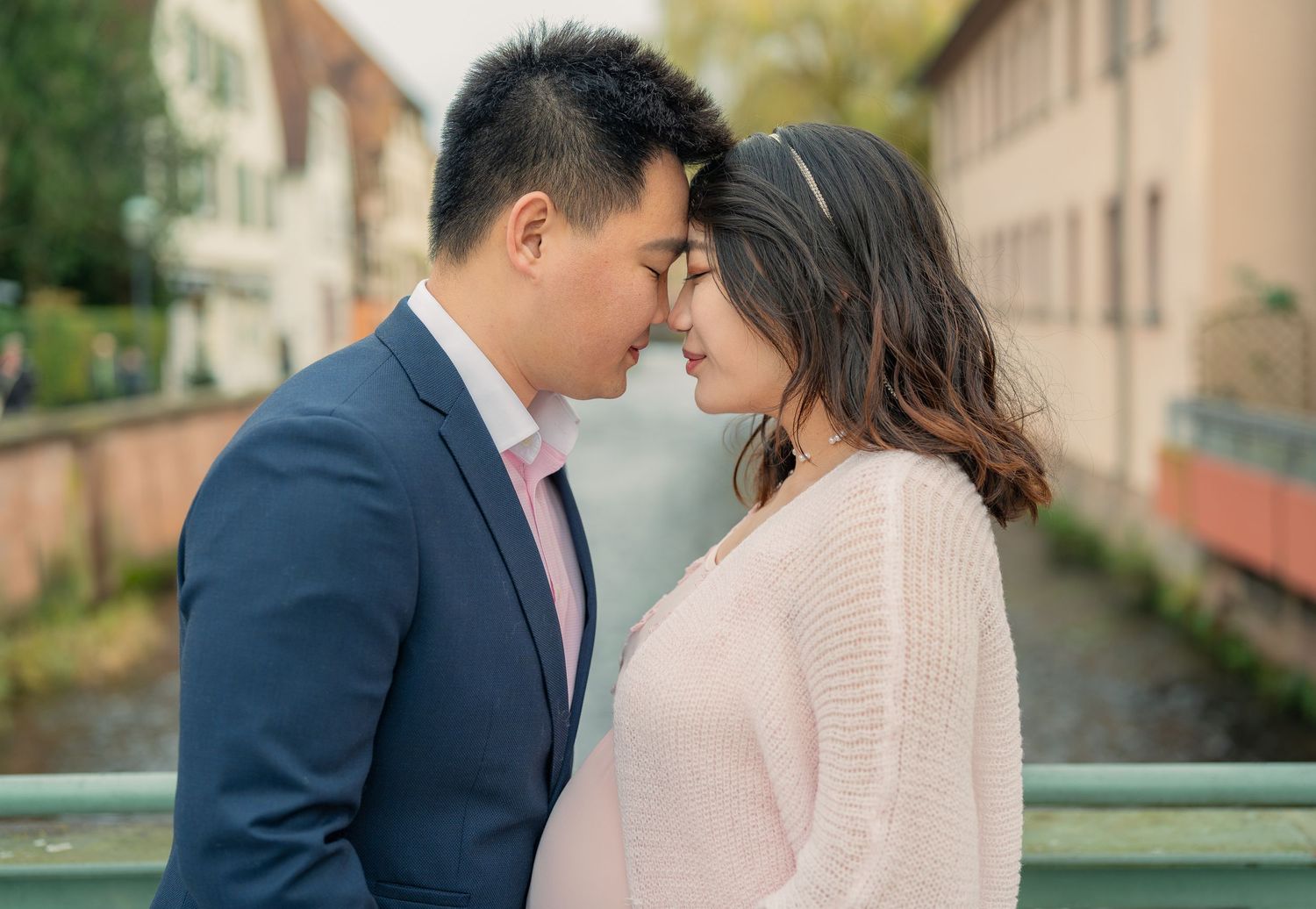 A romantic couple in formal attire share an intimate moment on a balcony overlooking buildings.