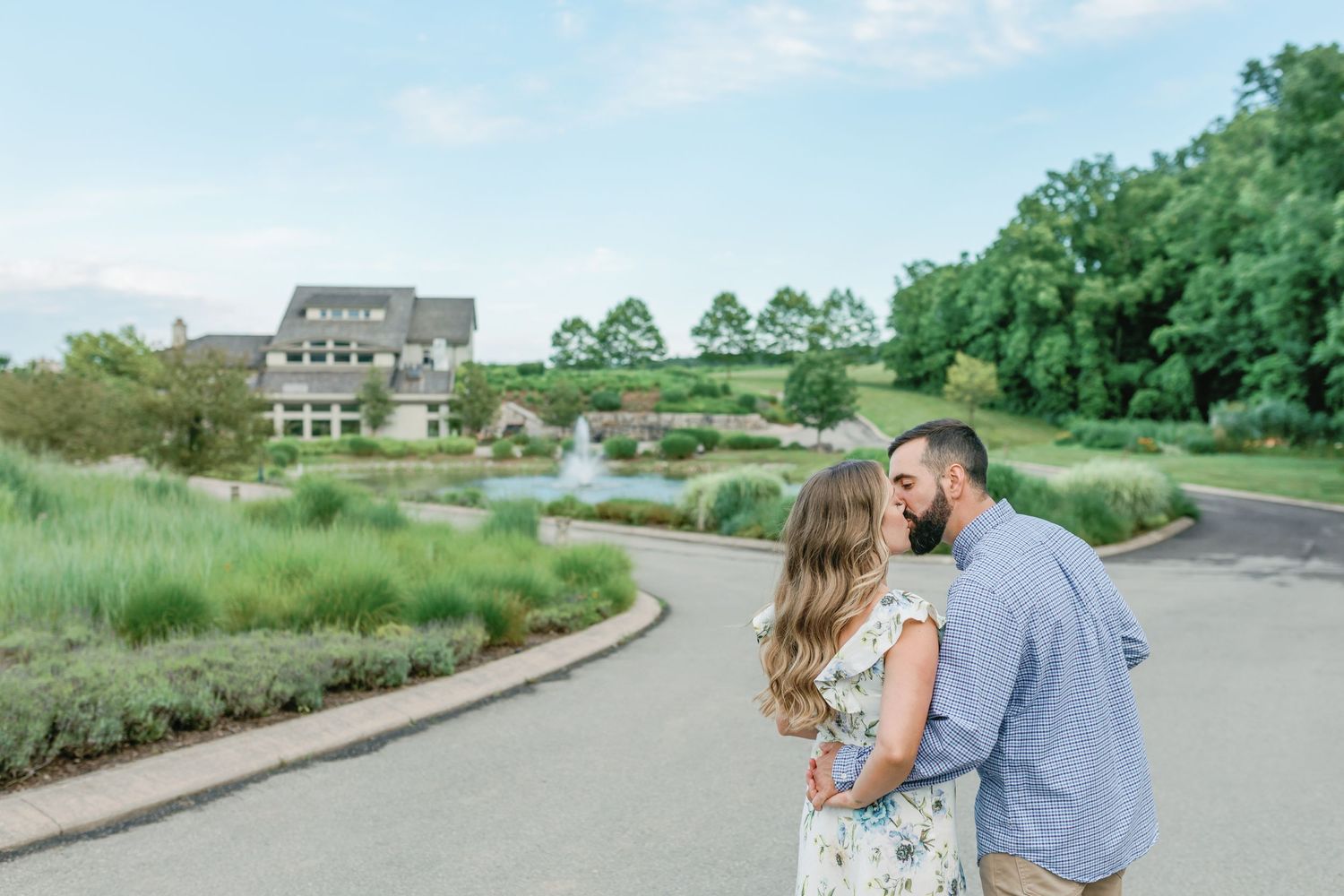 Couple walking together on a winding path with green scenery and buildings in the background.