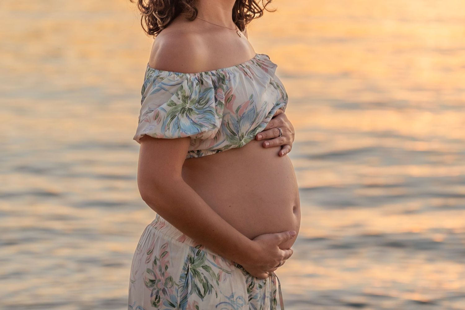 Maternity beach portrait during golden hour with waves in background.