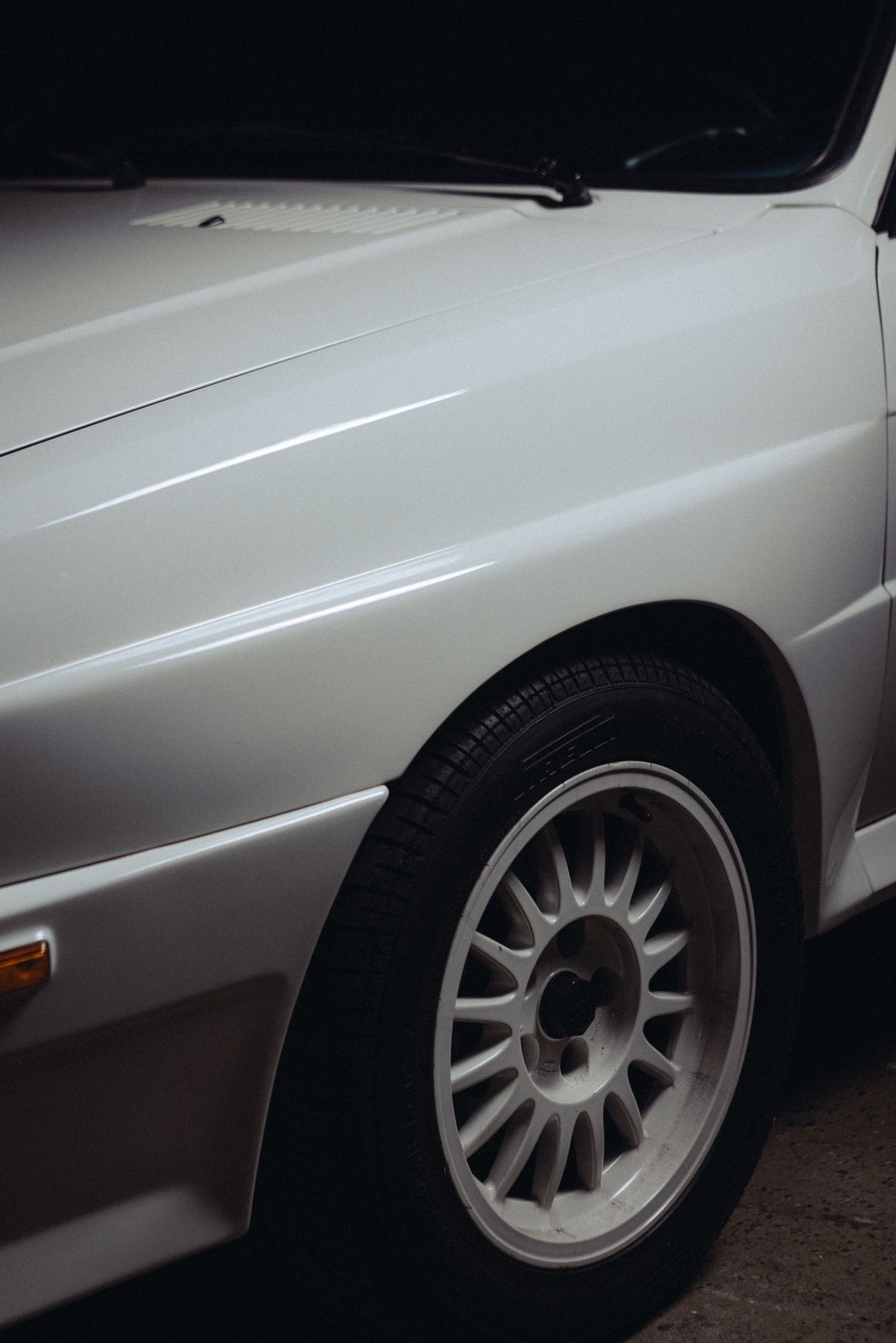 Close-up of a white classic car's fender and wheel with sunburst alloy design.