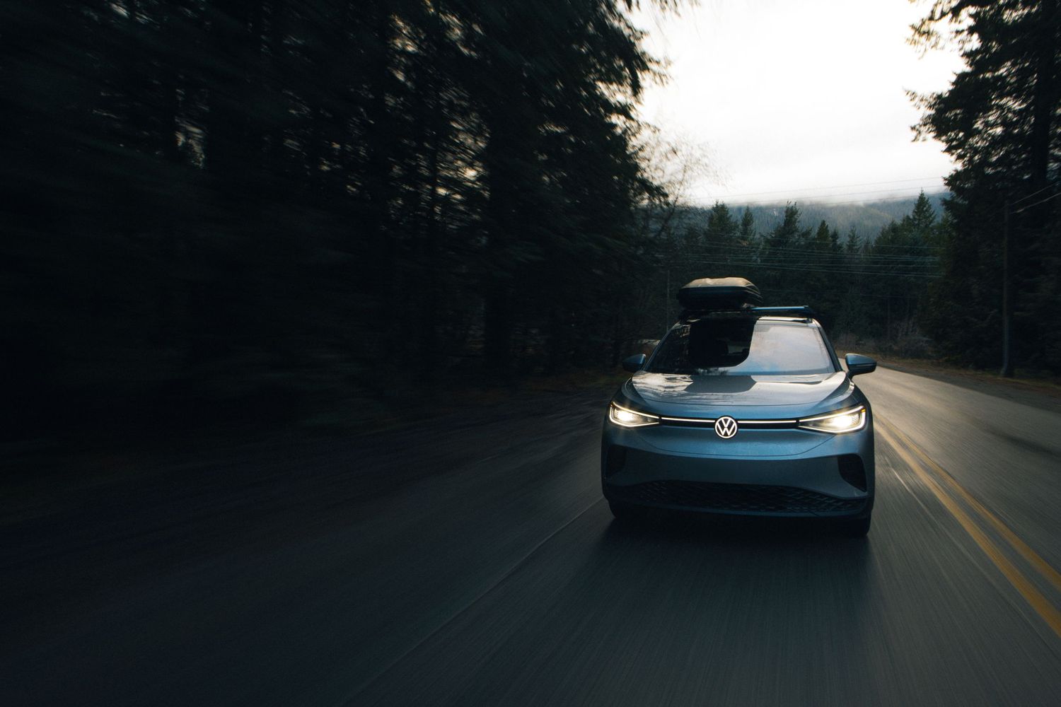 Blue Volkswagen driving on dark forest road with headlights illuminating the path.