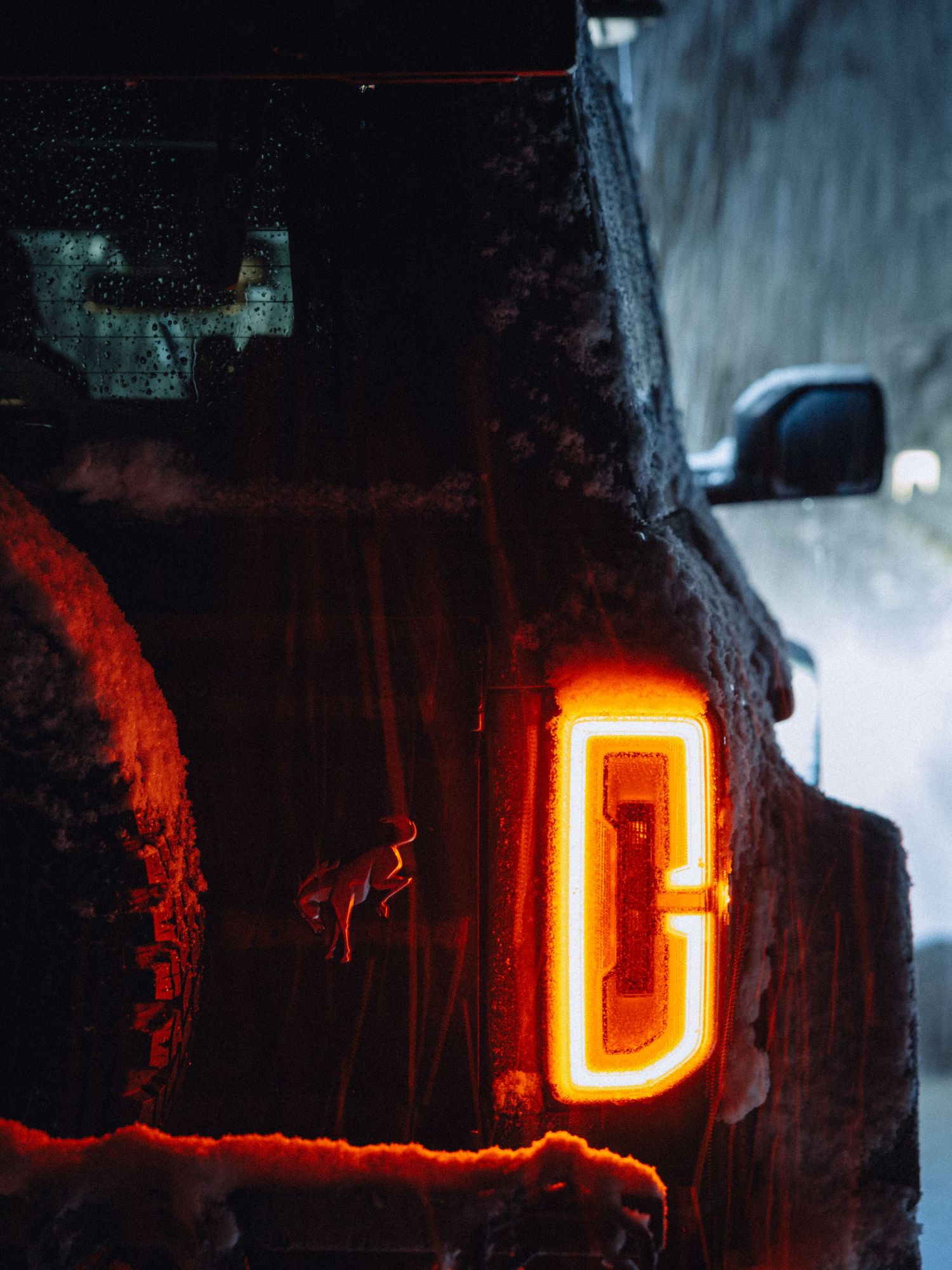 A glowing Ford Bronco taillight illuminates against a dark background during a snowy night.