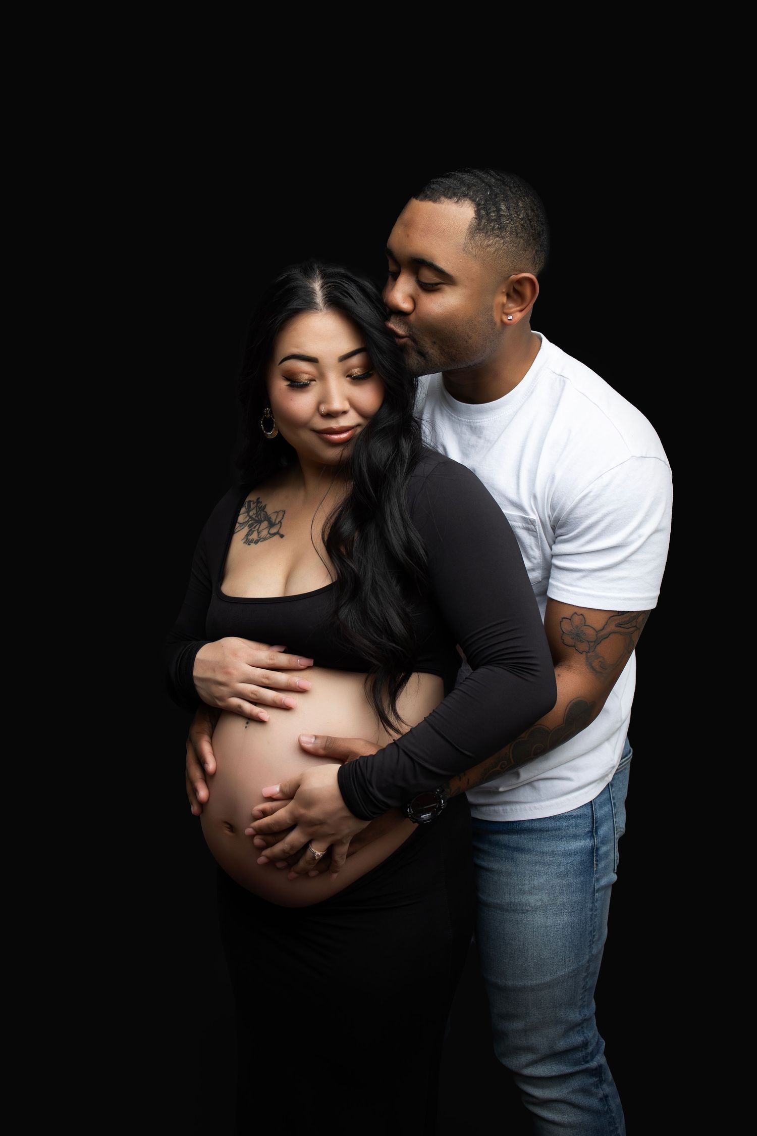 Intimate maternity photo with couple embracing against black background.