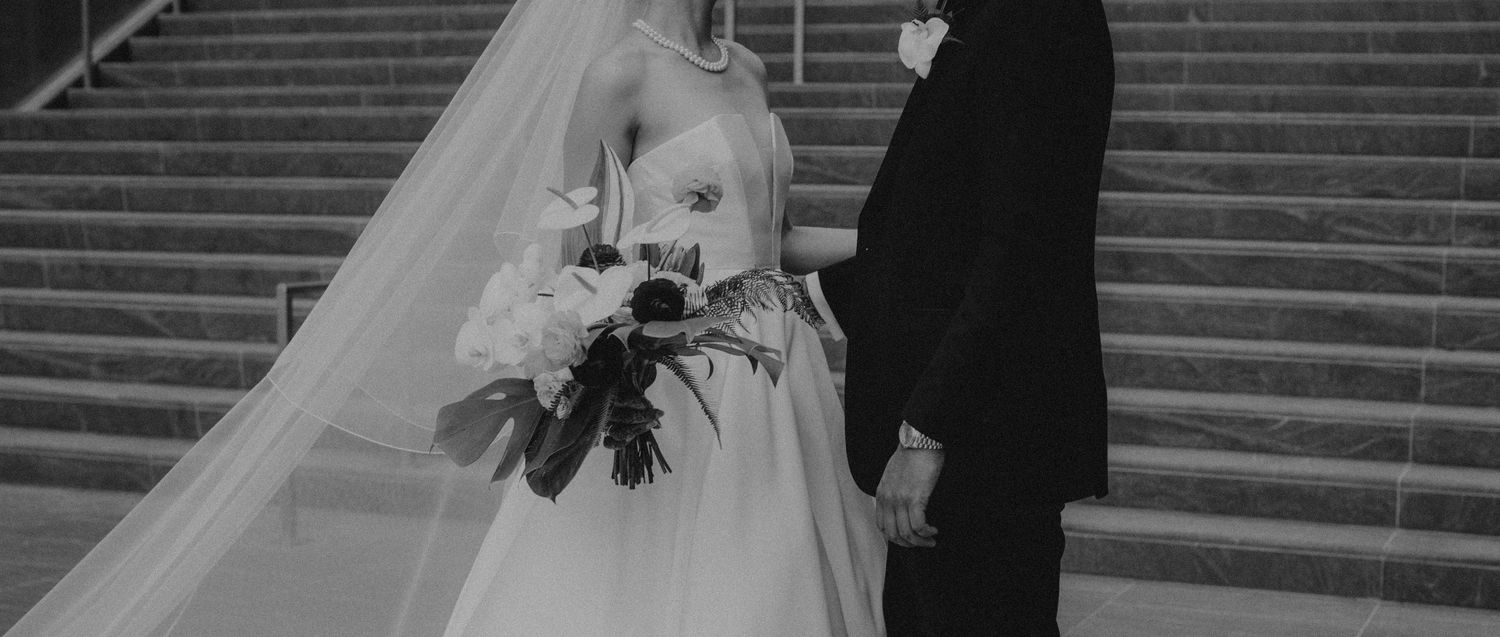 Black and white wedding photograph showing bride holding a bouquet of flowers as she stands on stone steps.