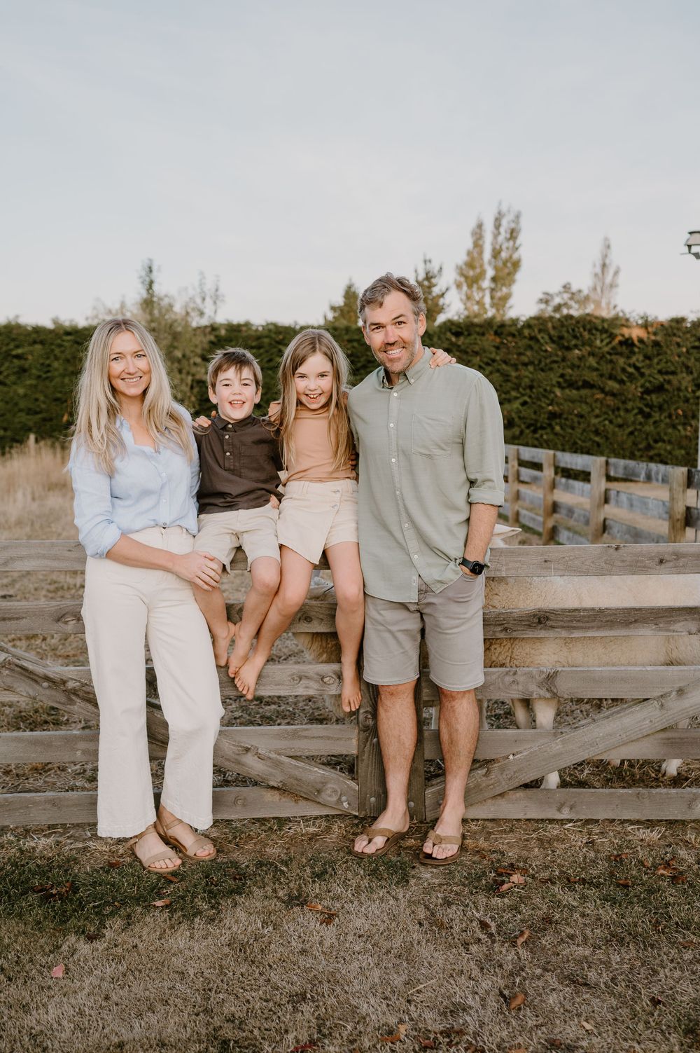 Small family group poses casually on wooden fence in outdoor setting.