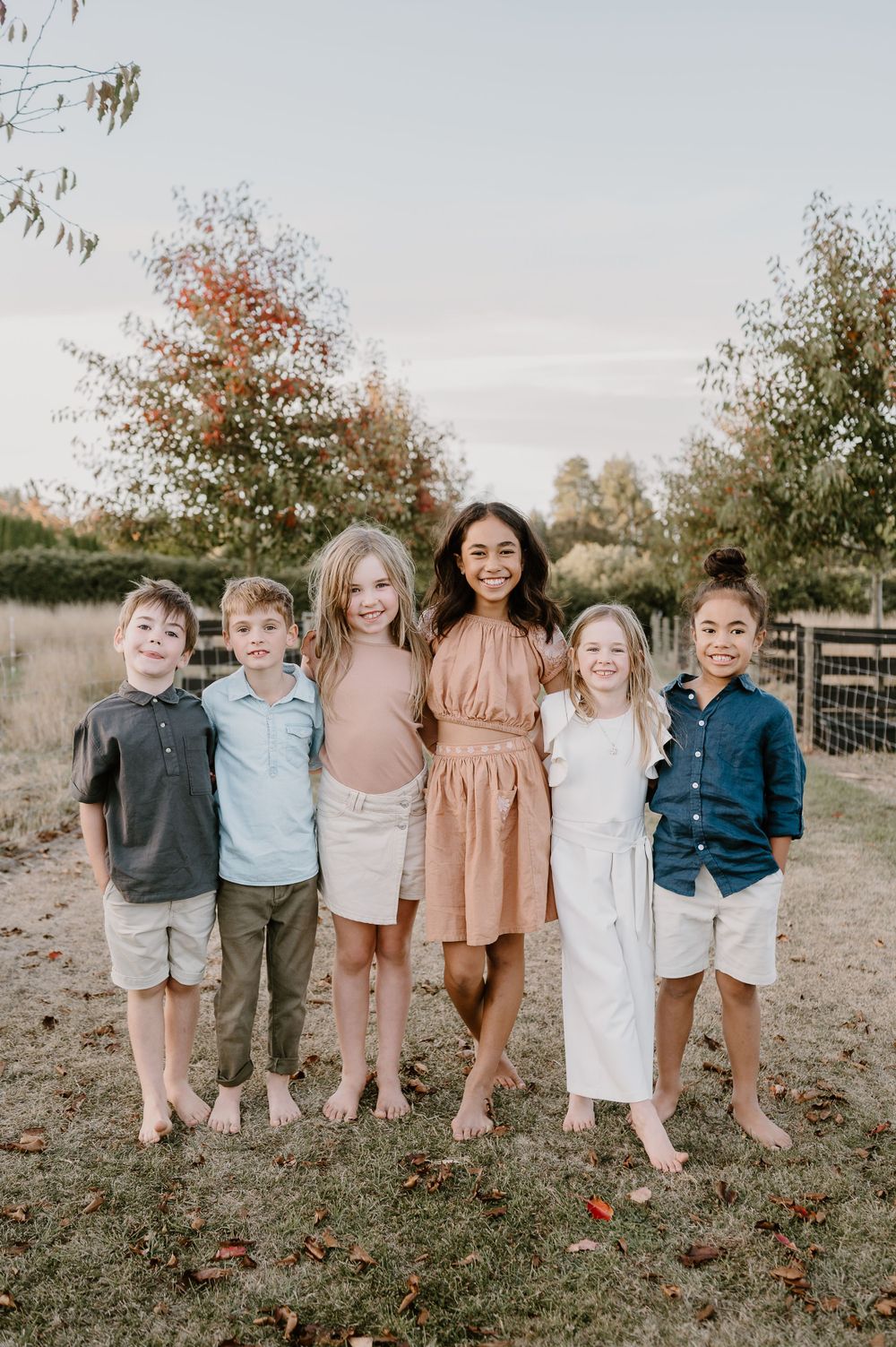 Children and adults pose together for a casual outdoor portrait on grass near a wooden fence.